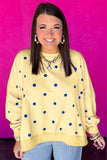 Smiling woman in pale yellow blue-dot sweatshirt & striped pants on pink wall.