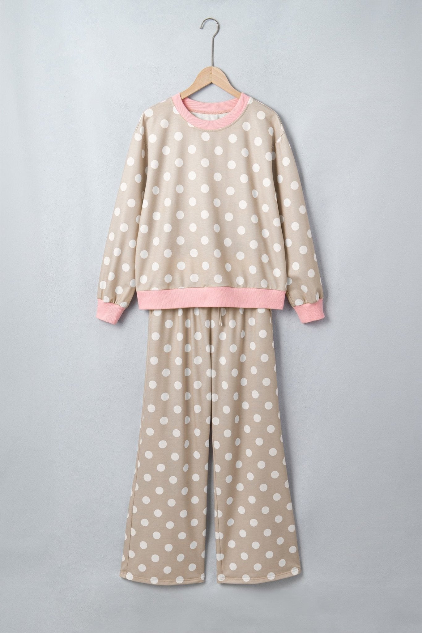 Beige polka-dot pajama set with pink trim, hanging on a wooden hanger.