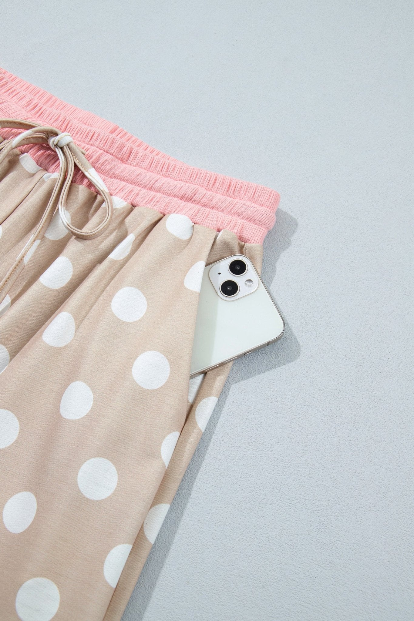 Close-up of beige polka-dot pajama pants with pink waistband and white smartphone in side pocket.
