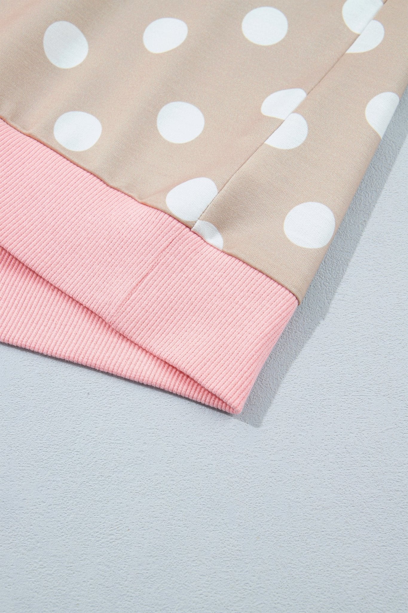 Close-up of beige polka-dot top with large white dots and pink ribbed crew neck on light gray.