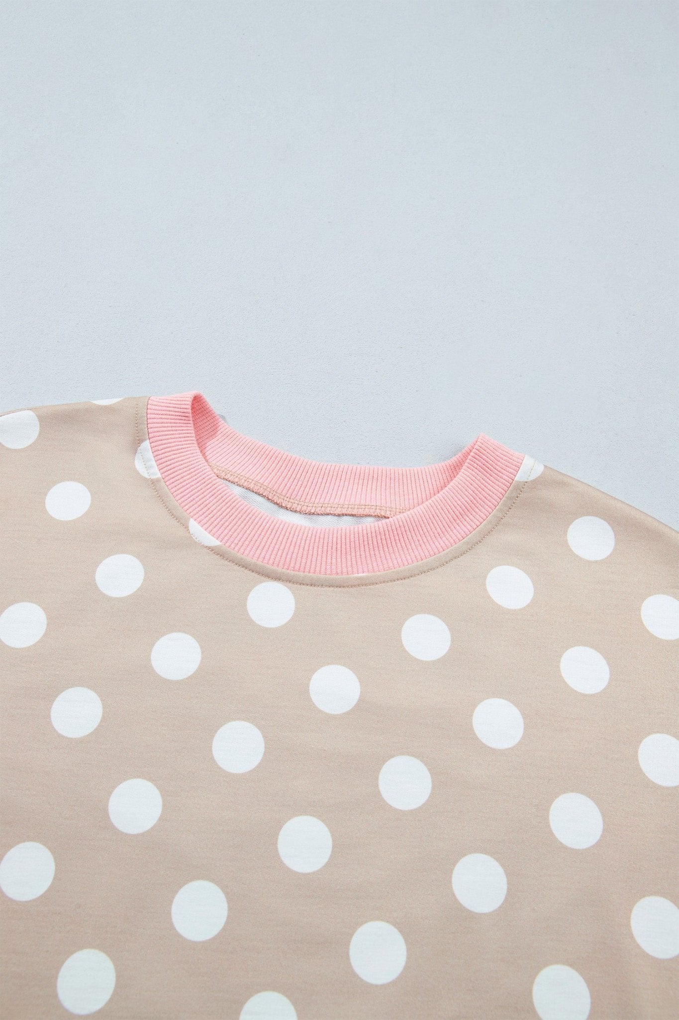 Close-up of baby sweatshirt with beige white-polka-dot body and contrasting light pink ribbed crew neck.