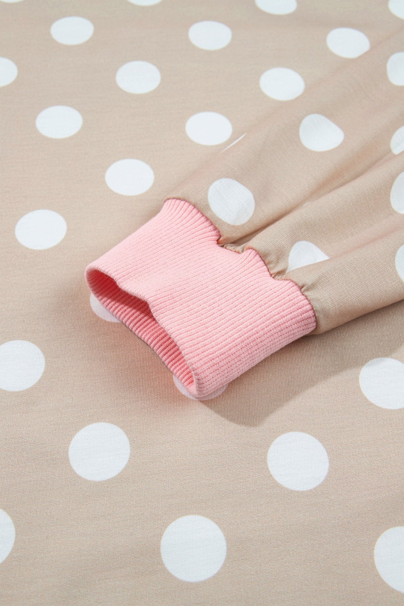 Close-up of beige polka-dot garment with white dots and contrasting pink ribbed cuff on matching fabric.