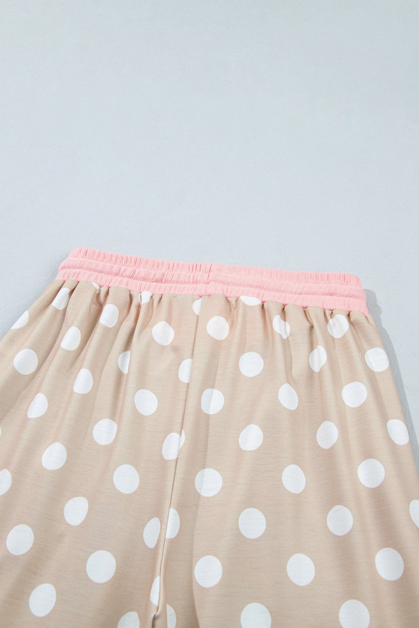 Close-up of beige polka-dot pajama pants with pink elastic waistband on a light gray background.