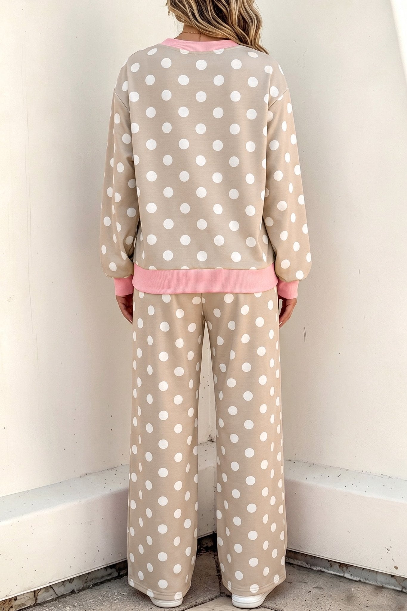 Back view of person in beige and white polka-dot lounge set with pink trim against off-white wall.