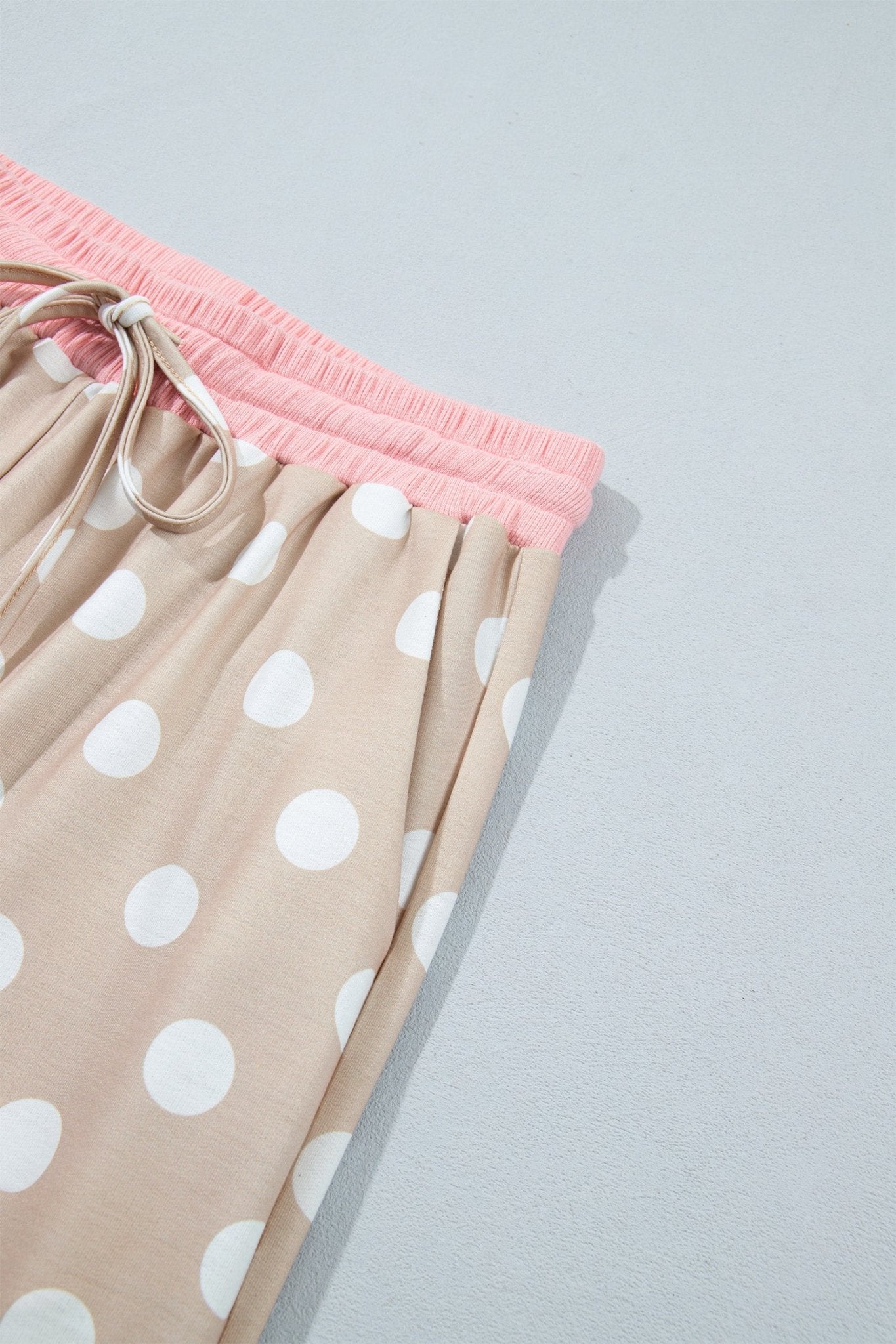 Close-up of beige polka-dot pants with bright pink elastic waistband and drawstring.