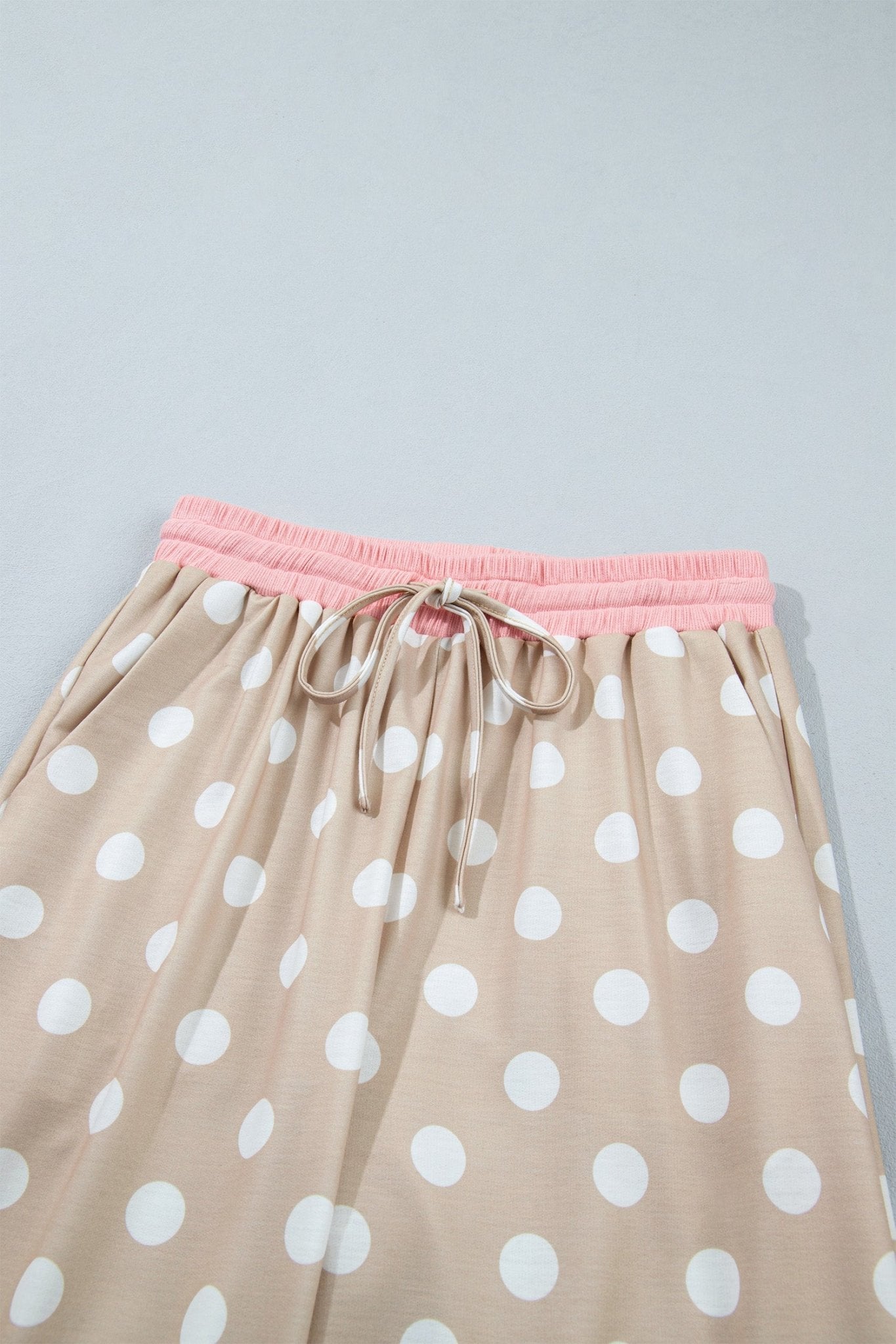 Beige-white polka-dot lounge pants with pink elastic waistband and drawstring on light gray.