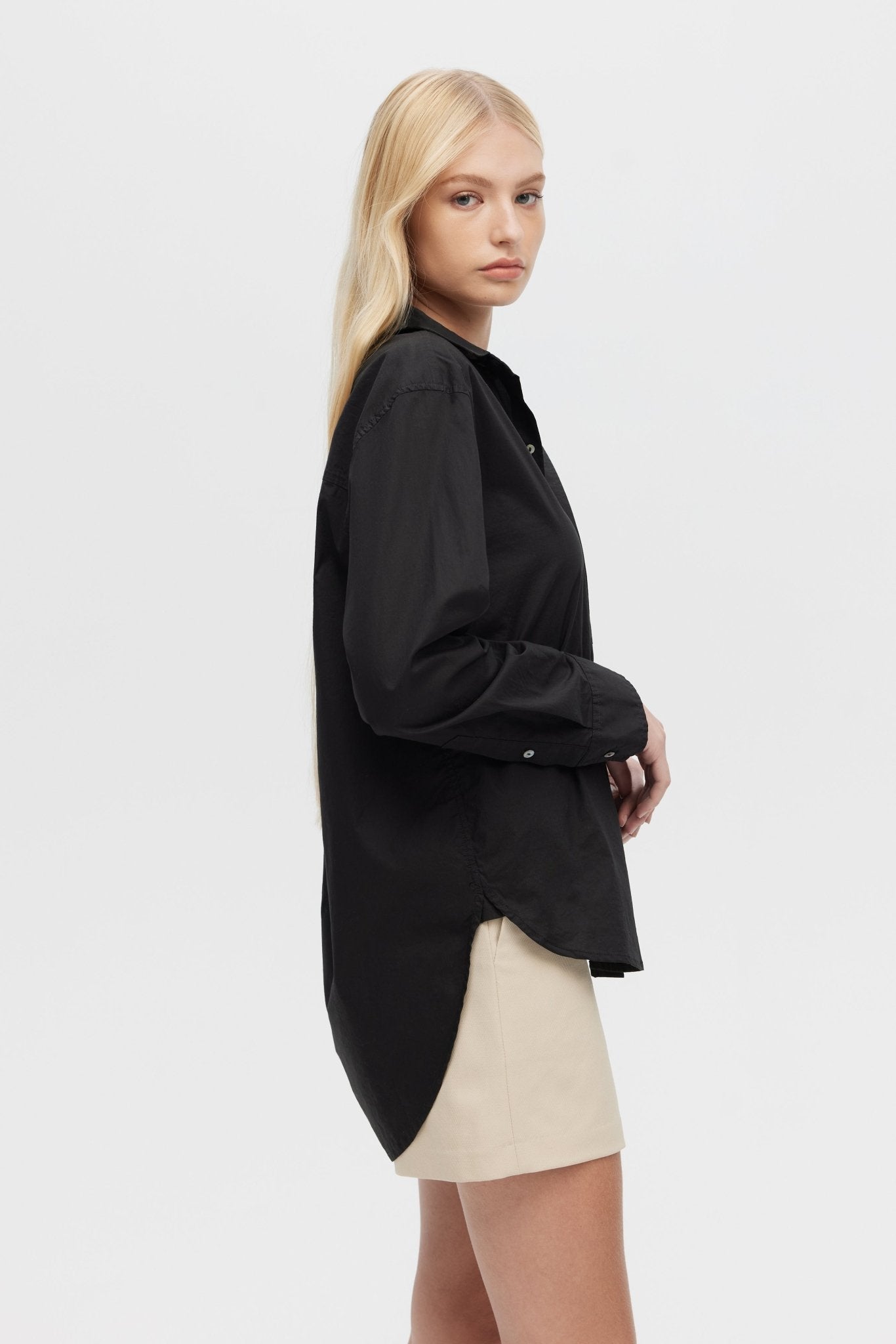Woman wearing a black oversized shirt over a beige skirt on a white background