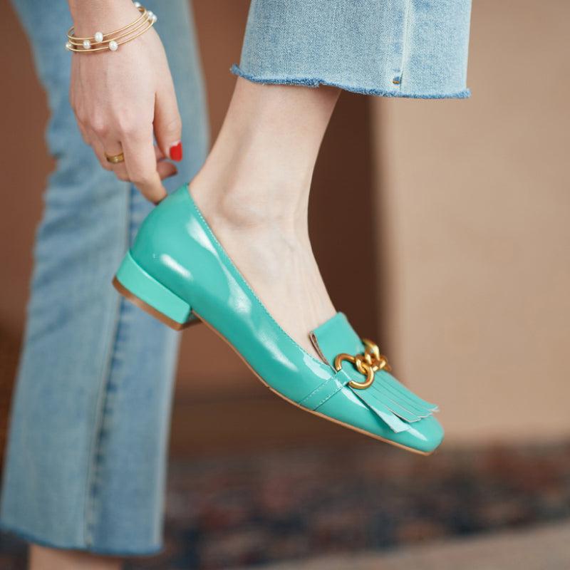 Teal patent leather shoe with gold buckle on a blurred background
