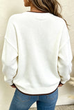 Woman wearing an oversized cream knit sweater with blue jeans against a light wall.