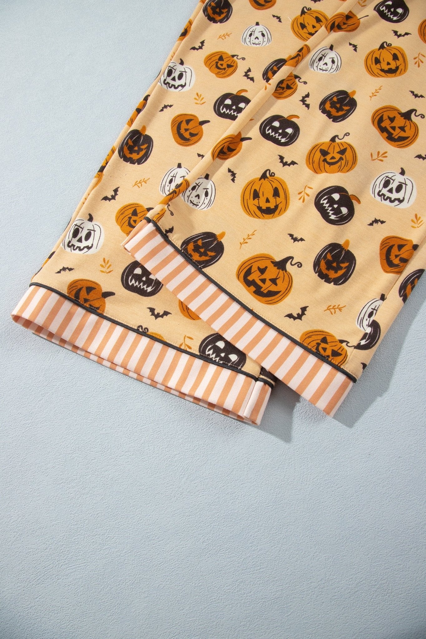 Close-up of beige Halloween fabric with pumpkins, bats, jack-o'-lanterns, and striped border.