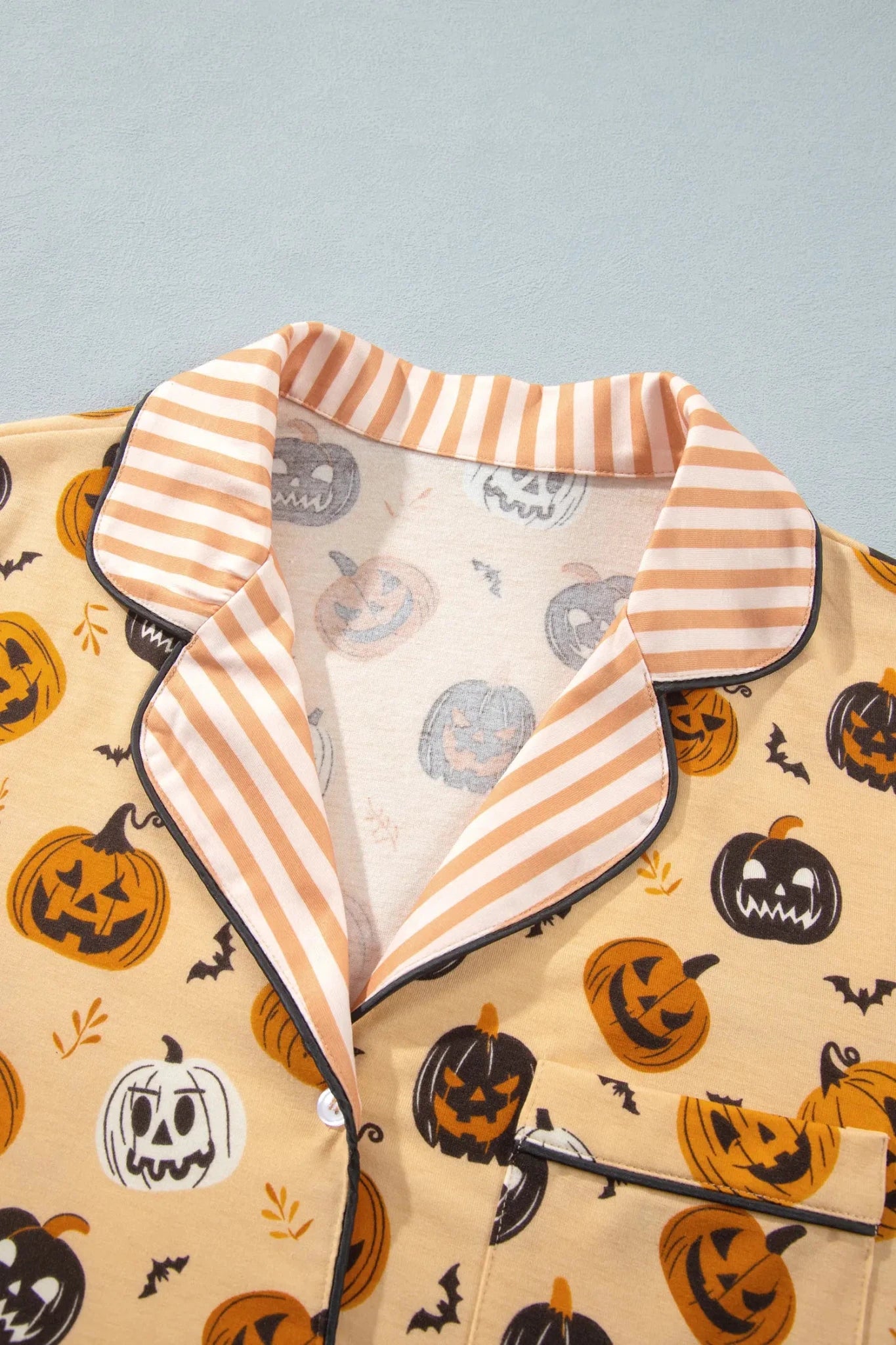 Beige Halloween pajama top with pumpkin print and striped collar.