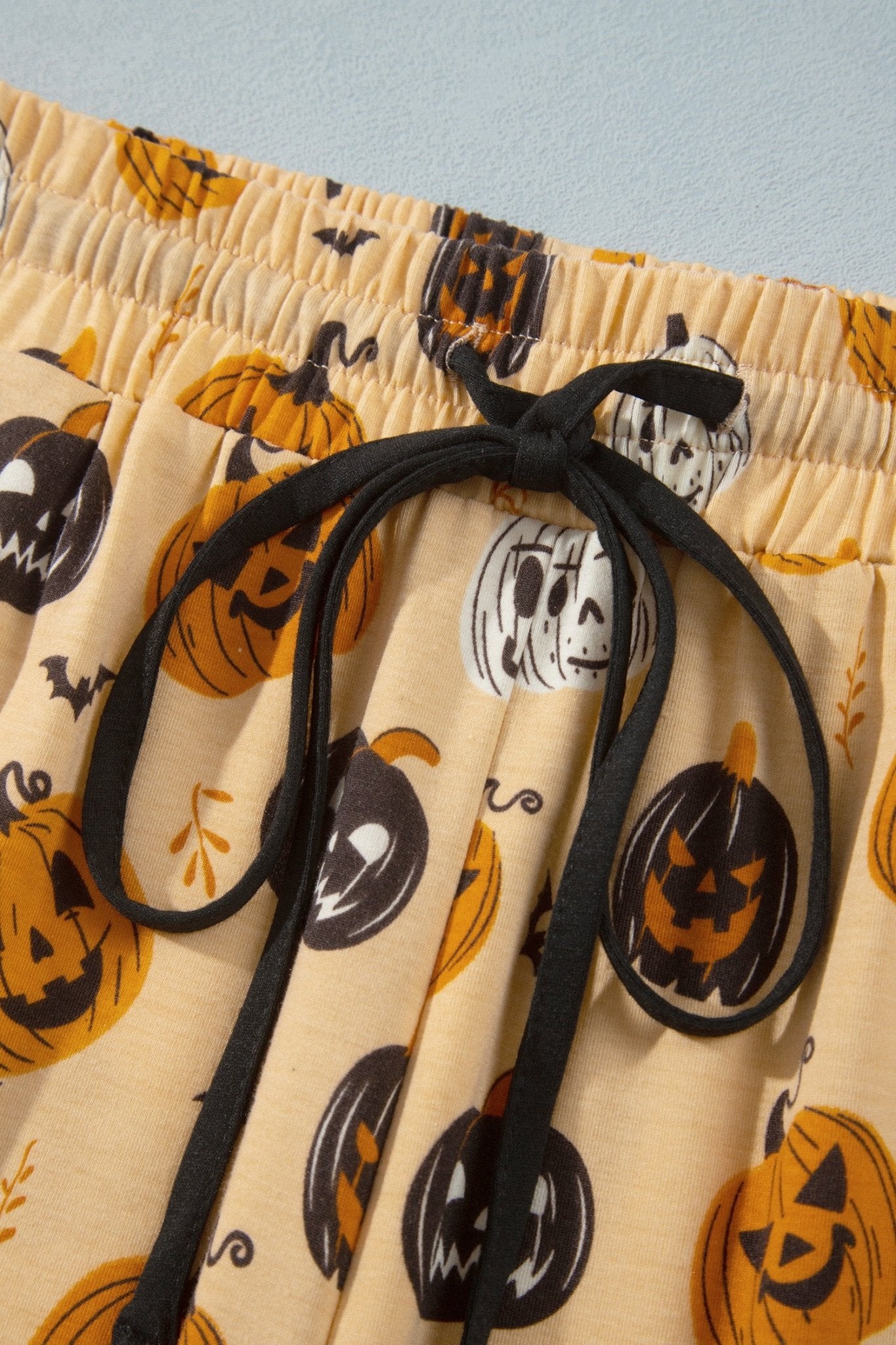 Beige Halloween shorts with jack-o'-lantern, bat, and skull prints, elastic waist.