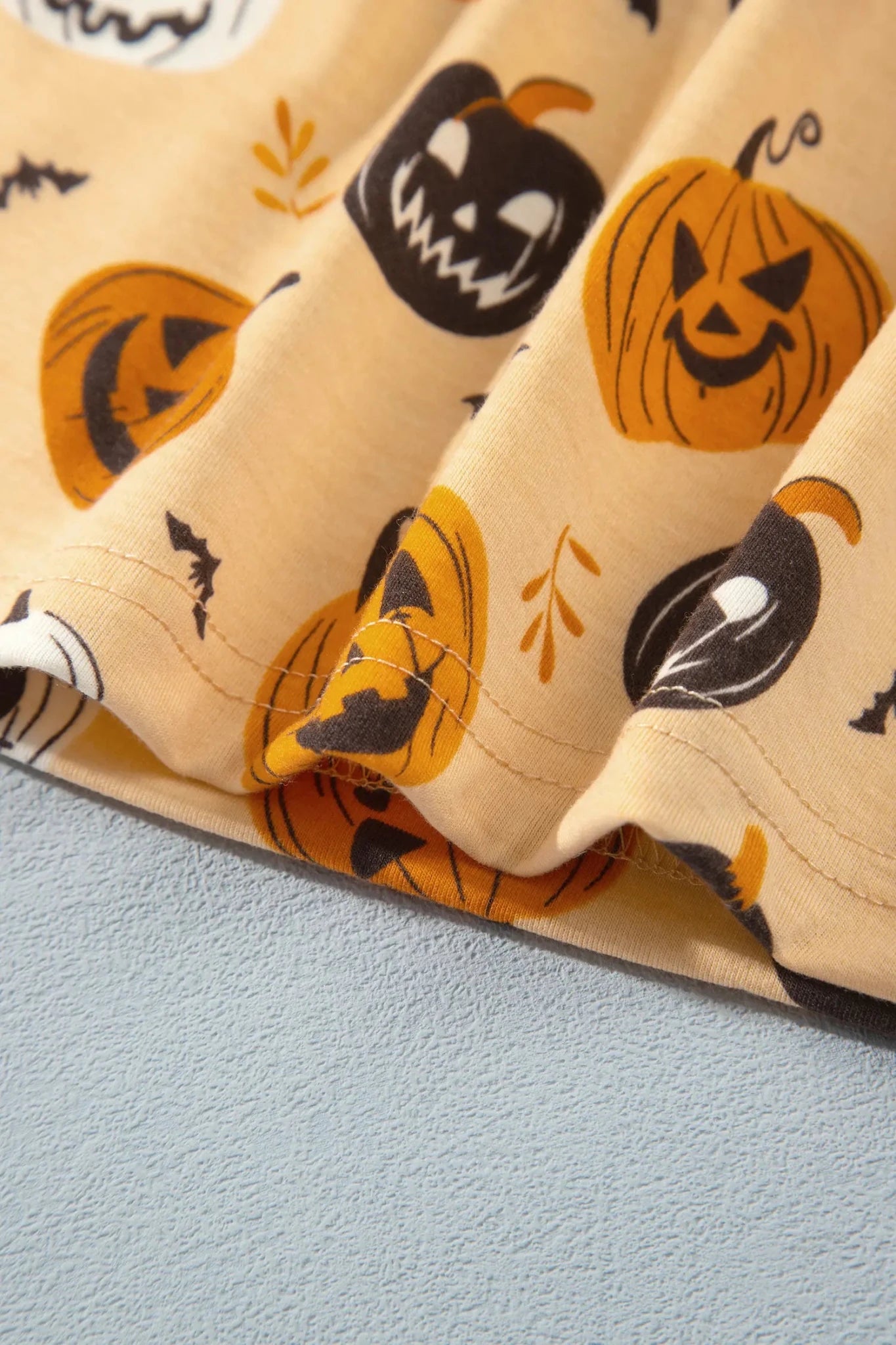 Beige Halloween fabric with pumpkins, bats, and orange leaves.