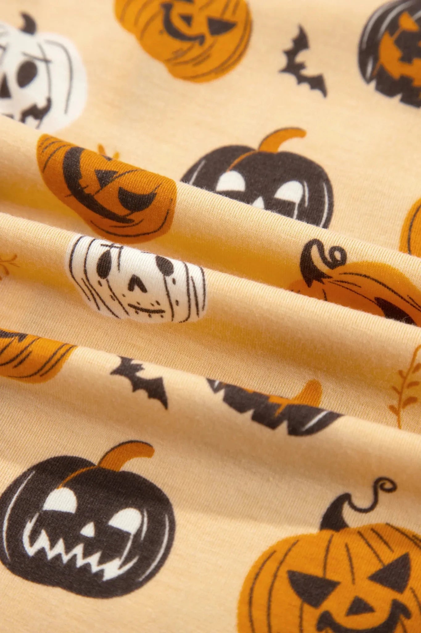 Beige Halloween fabric with pumpkins, skulls, and black bats.