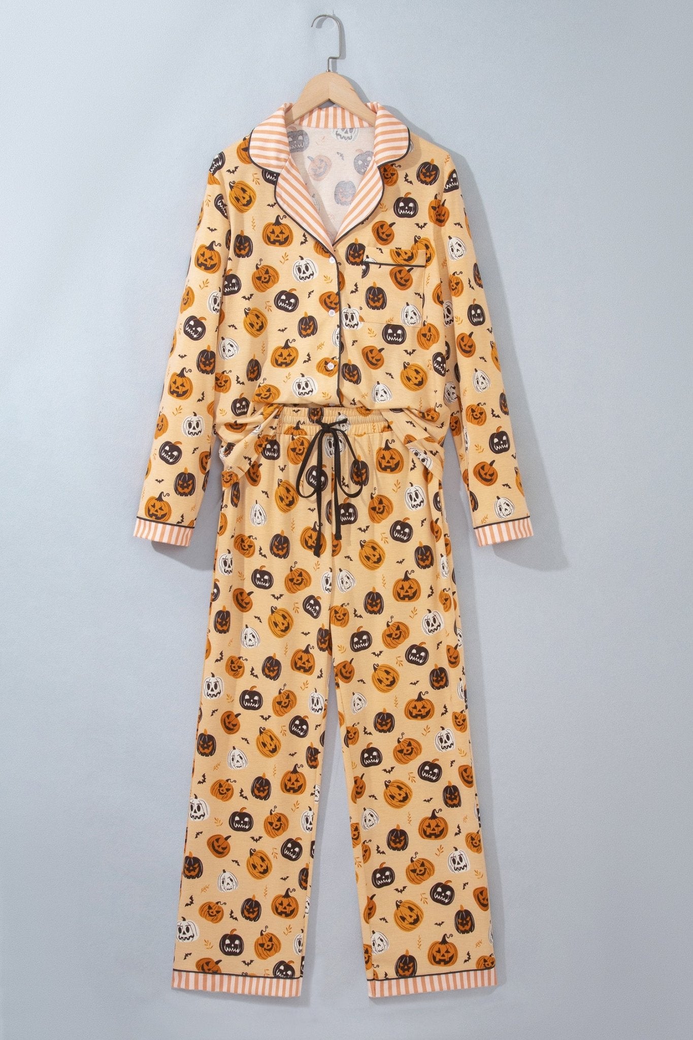 Beige Halloween pajama set with pumpkins, jack-o'-lanterns, and ghost prints on a hanger.