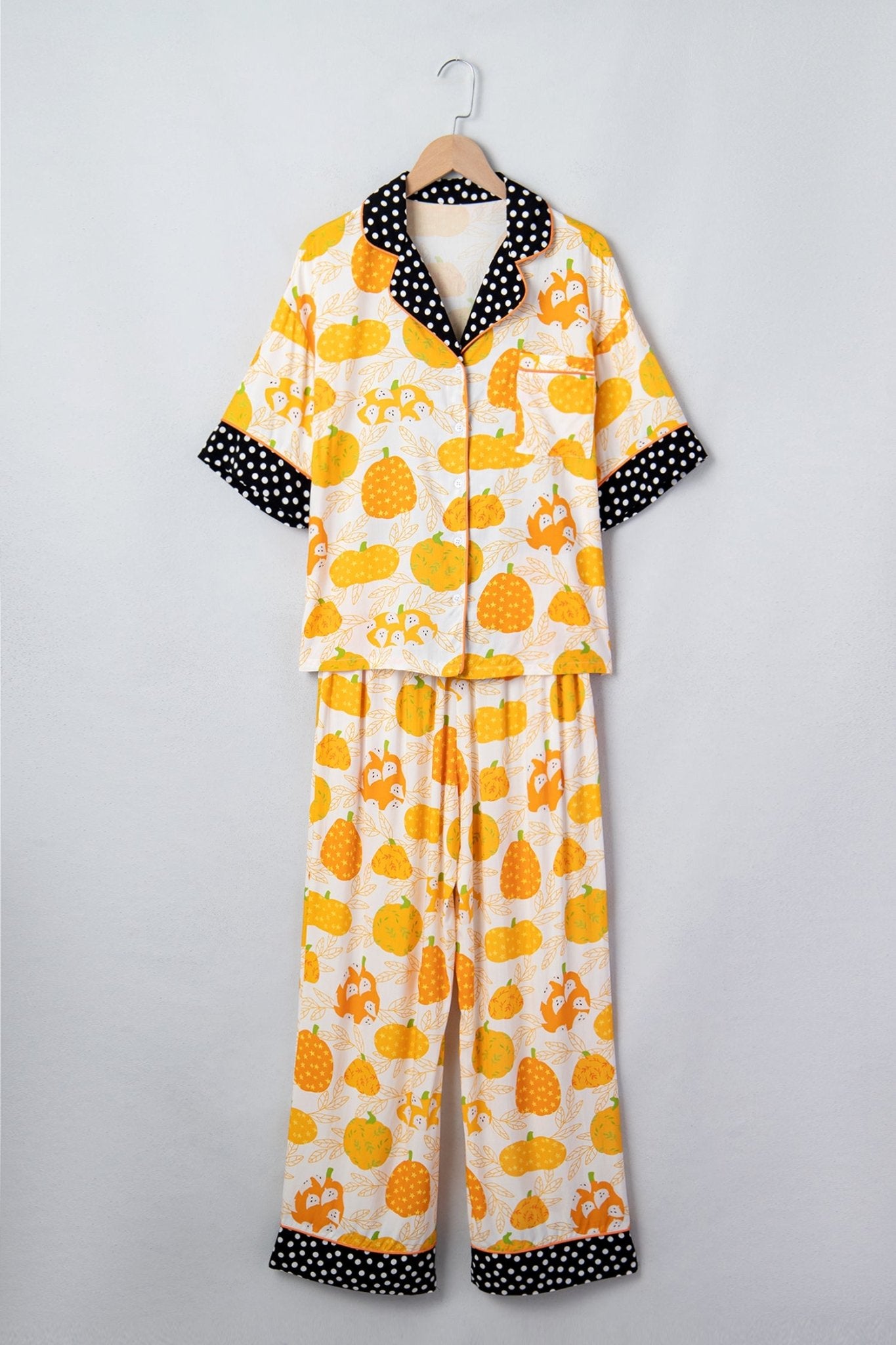 Cream pumpkin-print pajamas with black-and-white polka-dot trim on hanger.
