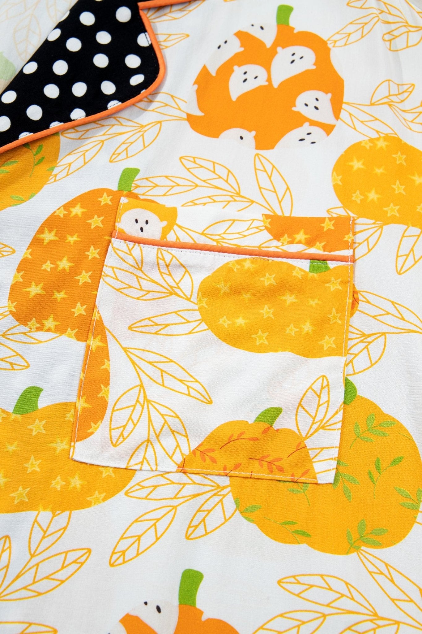 Close-up of white pumpkin-print fabric with stitched pocket and polka-dot trim.
