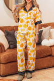 Woman in yellow and orange pumpkin-print pajamas by a brown leather couch.
