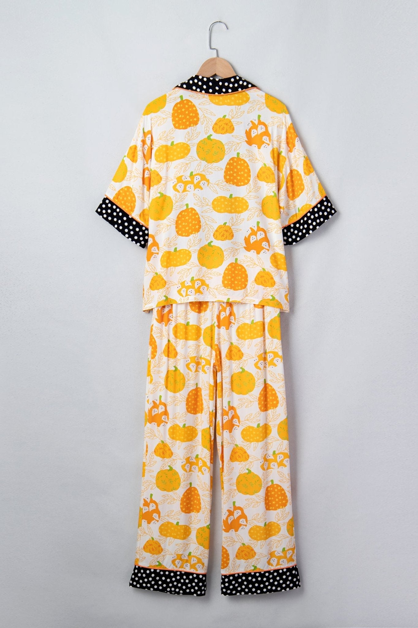 Cream pumpkin-print pajama set with black-and-white polka-dot trim on hanger.
