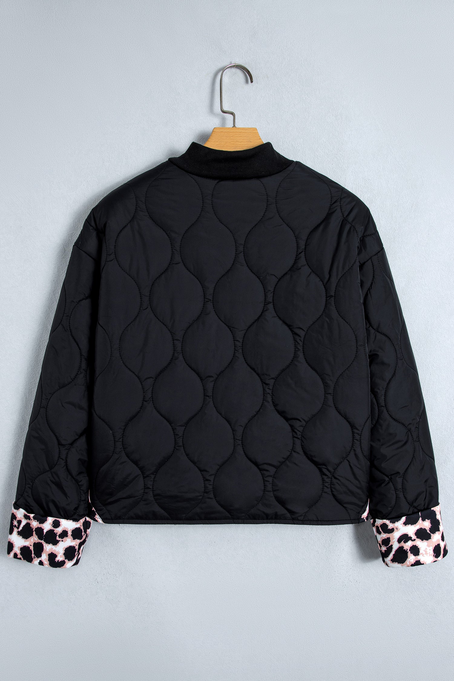 Black quilted puffer jacket with stand collar on a hanger, back view