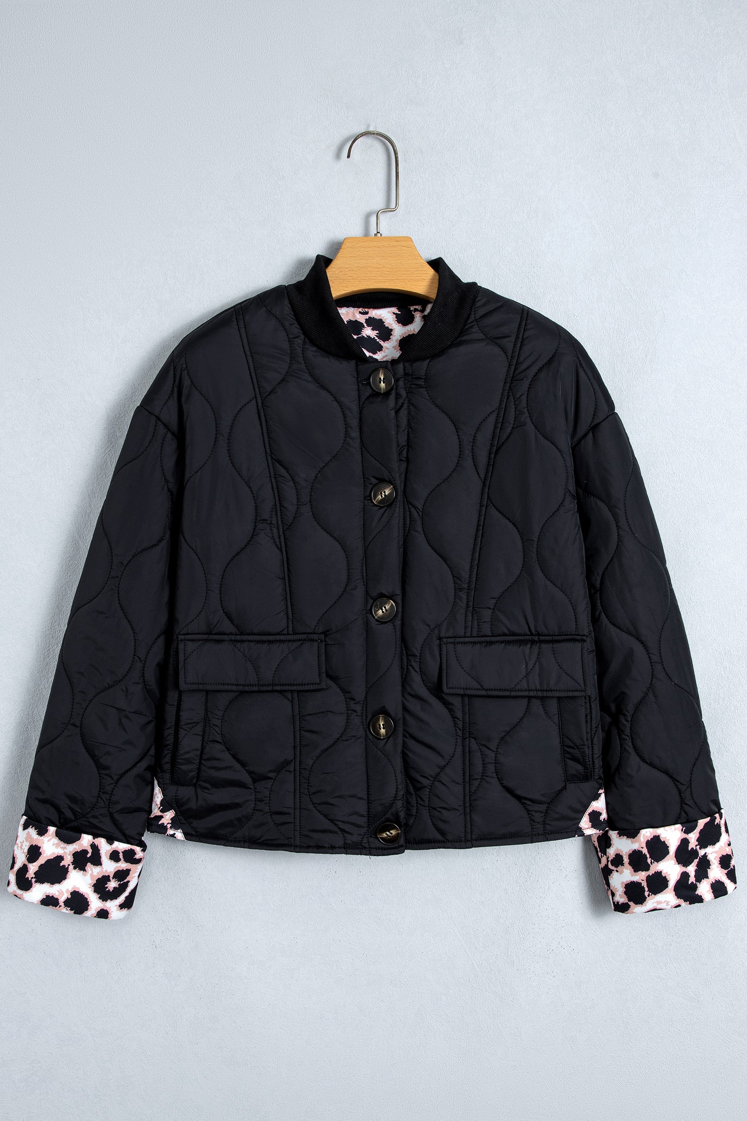 Black quilted puffer jacket with leopard cuffs on a hanger, front view