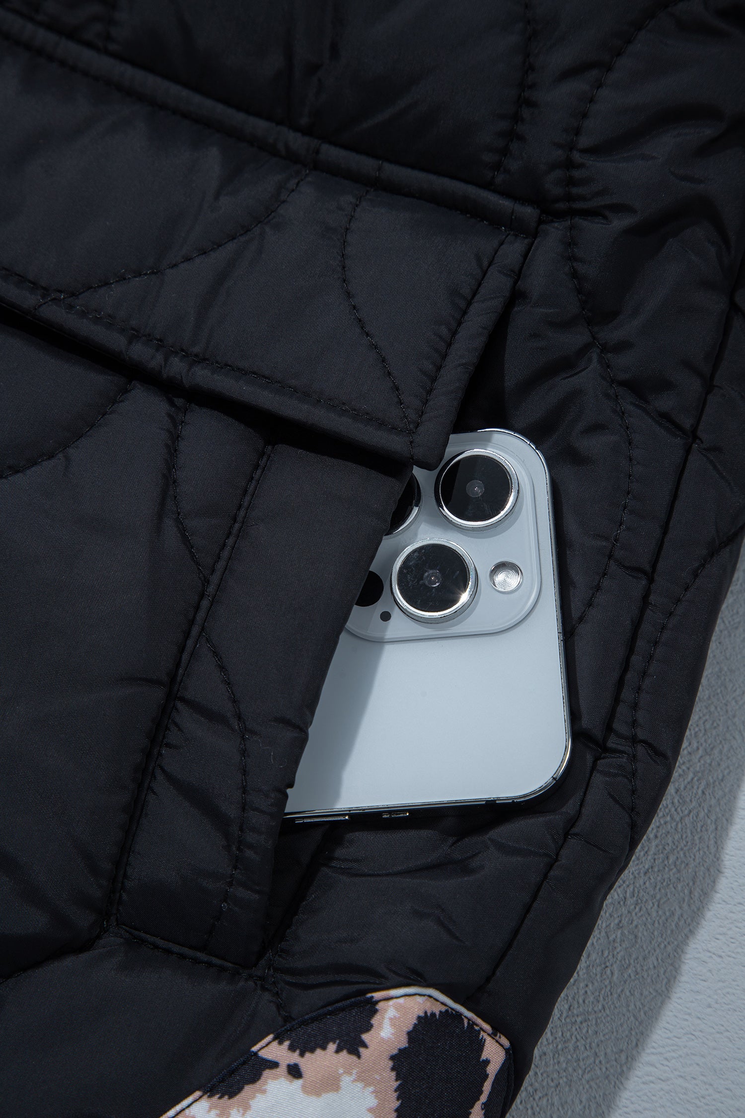 Black quilted jacket flap pocket holding a phone