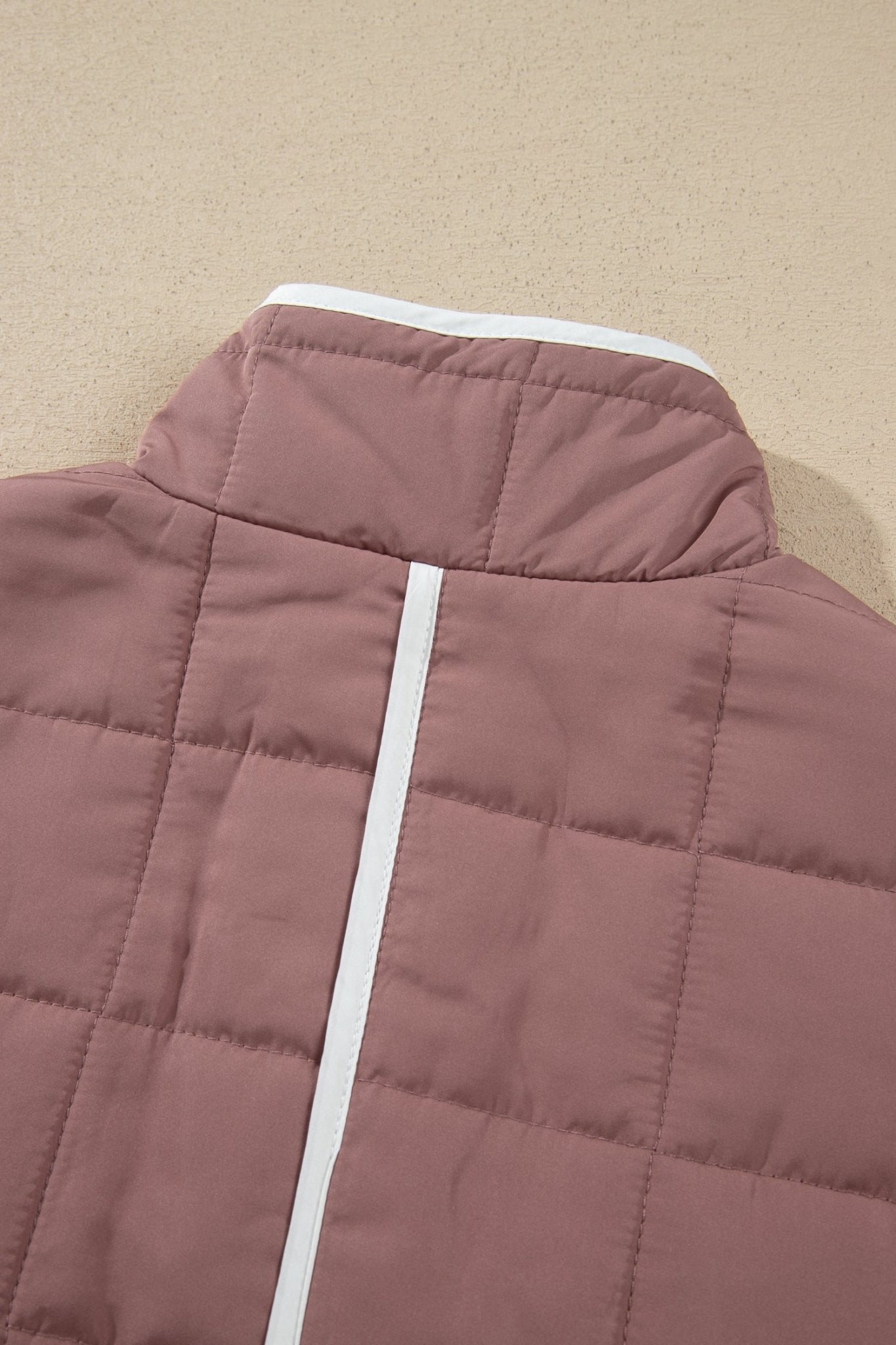 Close-up of dusty rose quilted puffer jacket back with high collar and white center zipper.