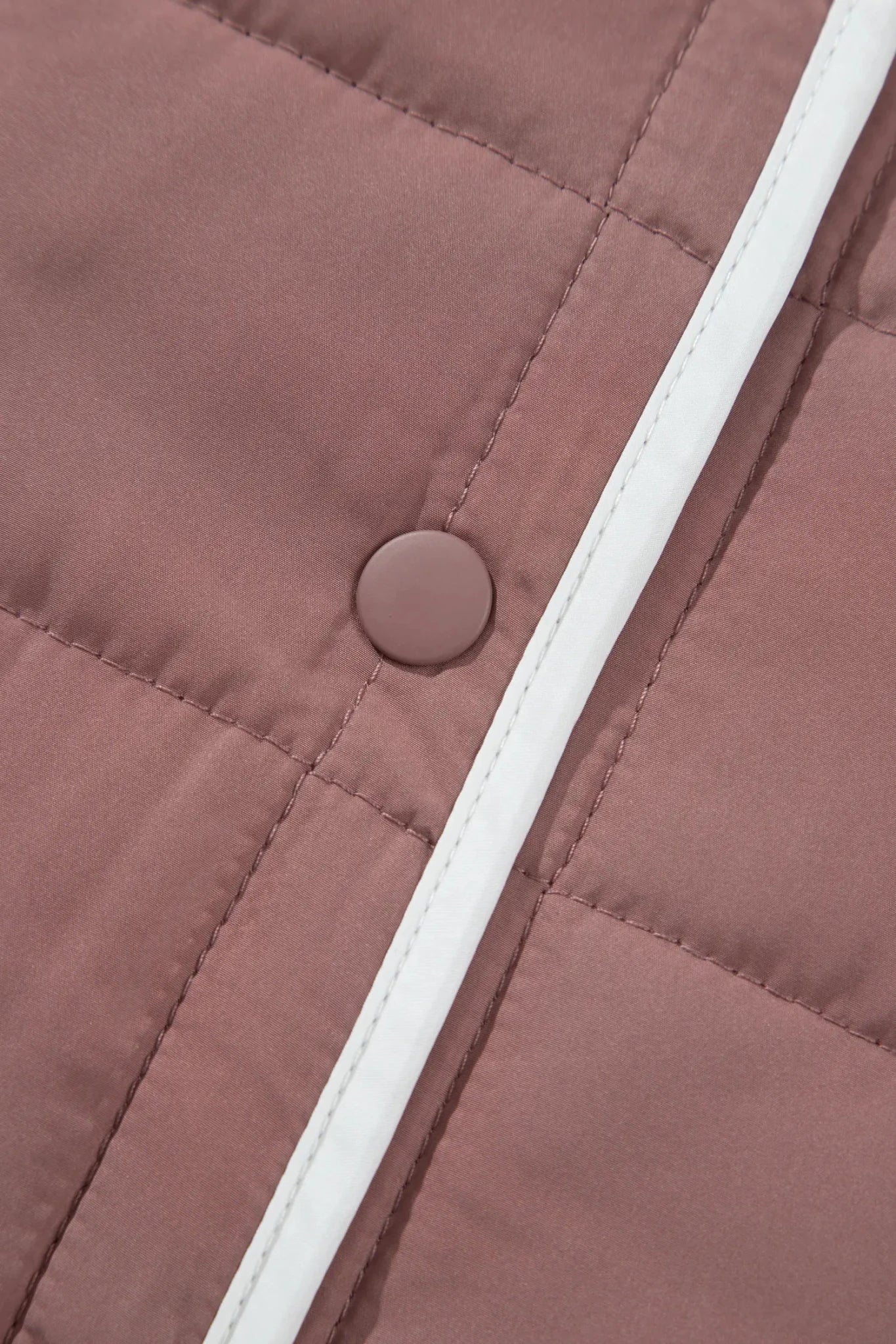 Close-up of a dusty rose quilted jacket featuring a matching fabric snap button and a contrasting white piping trim.