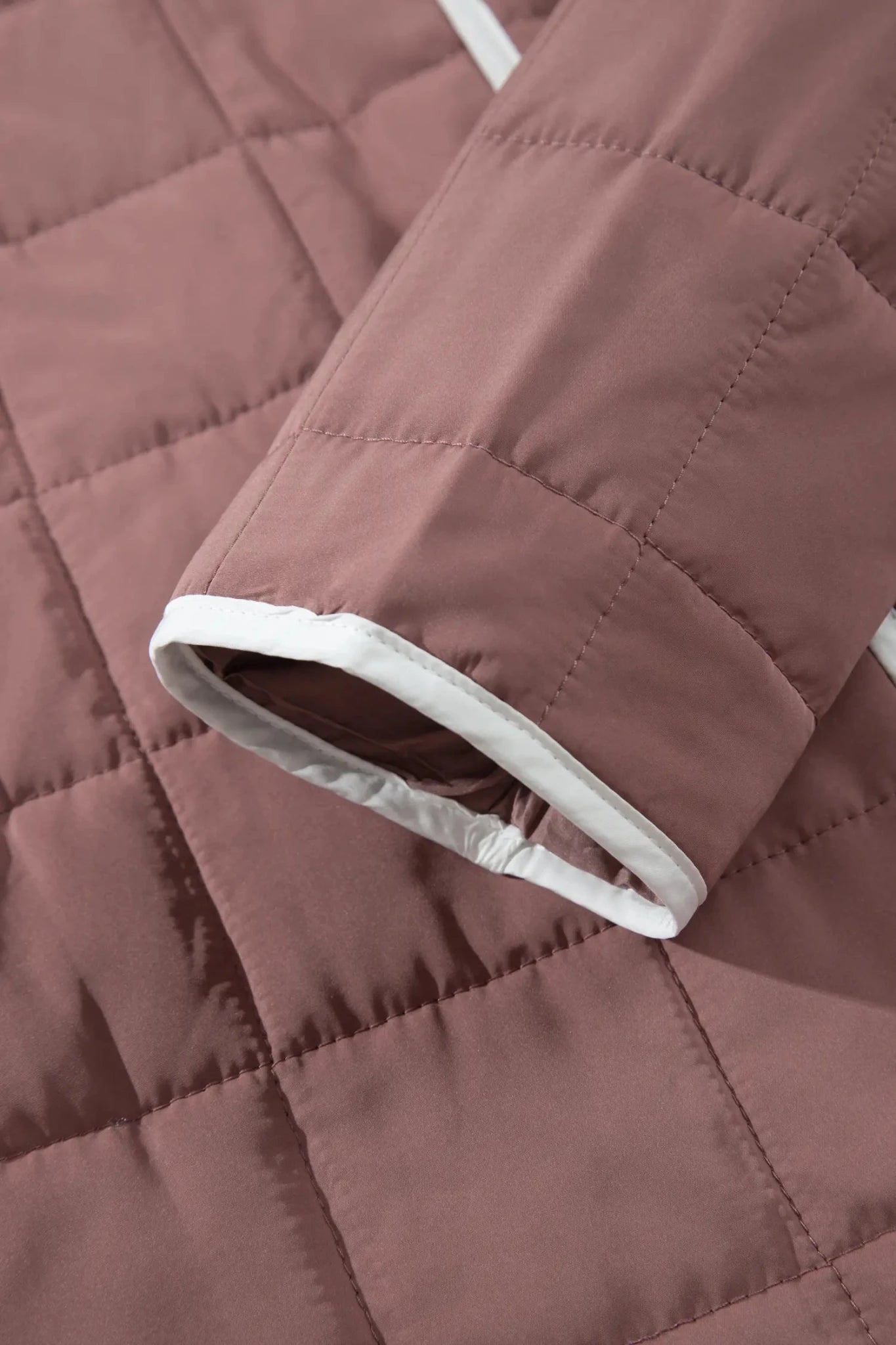 Close-up of a quilted dusty rose jacket sleeve with a white ribbed trim.