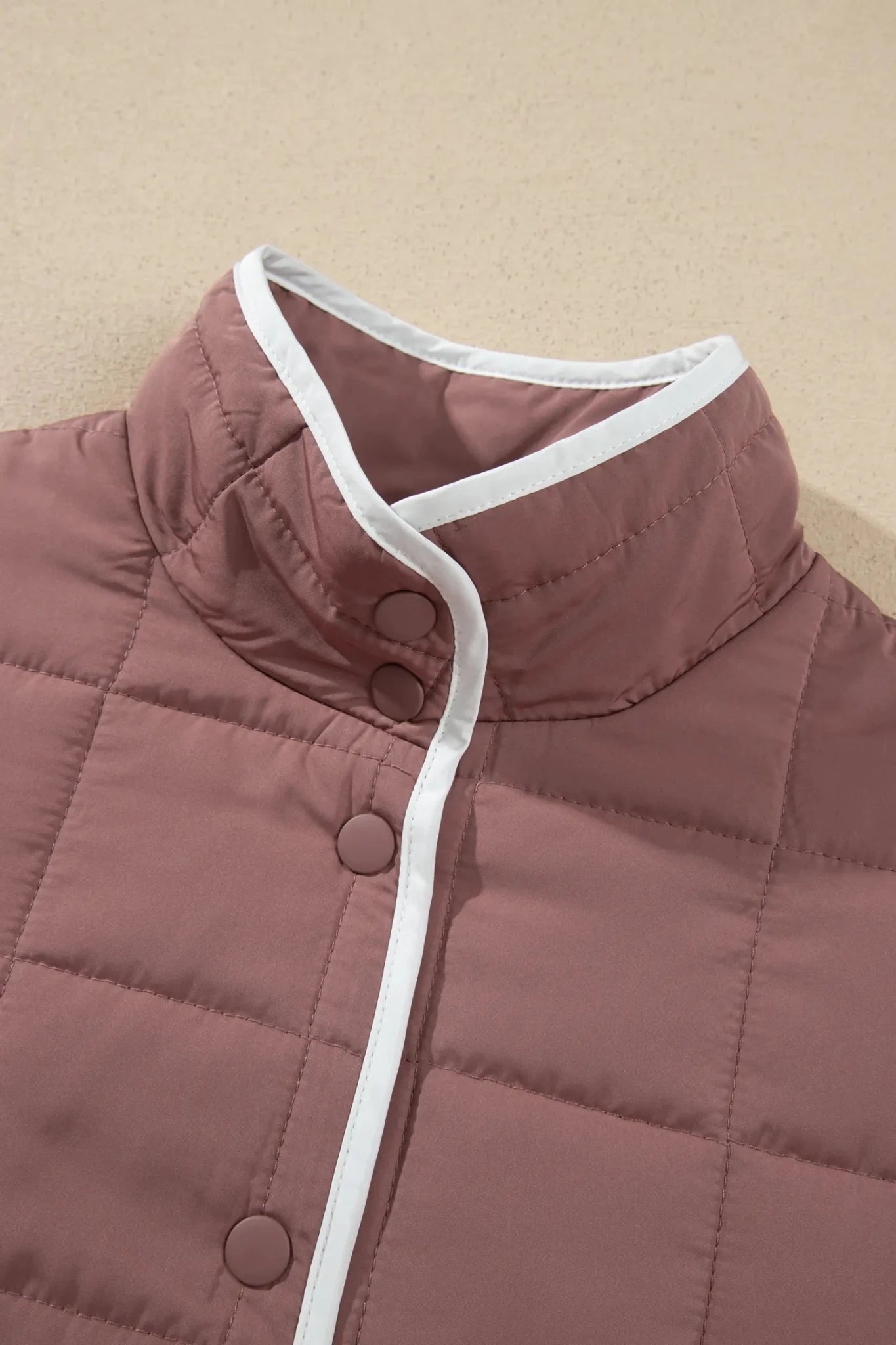 Close-up of dusty mauve quilted puffer jacket with white-trimmed collar and snap closure.