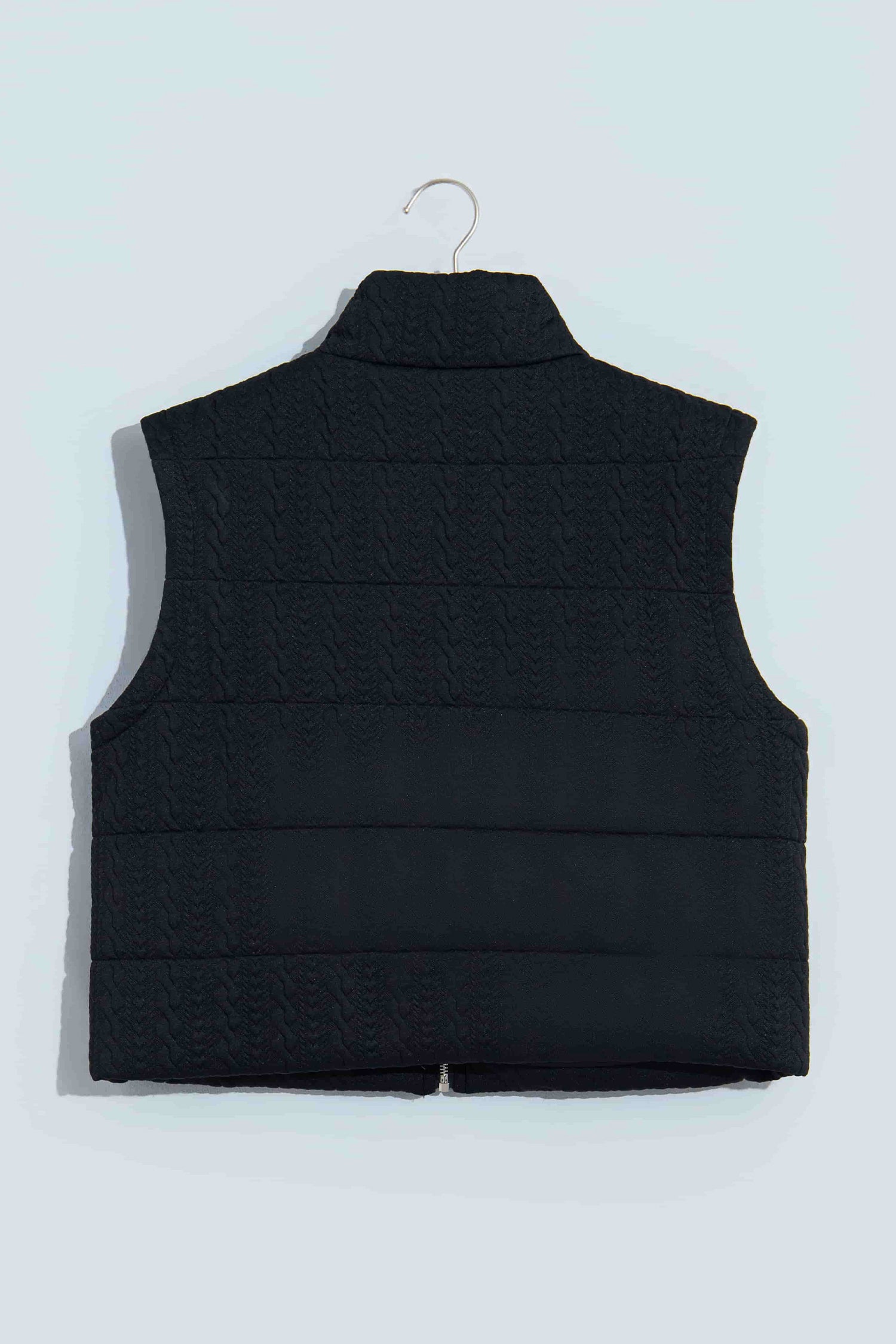 Black quilted zip up vest on a hanger, back view