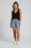 Woman wearing a black tank top with embellishments and denim shorts on a white background