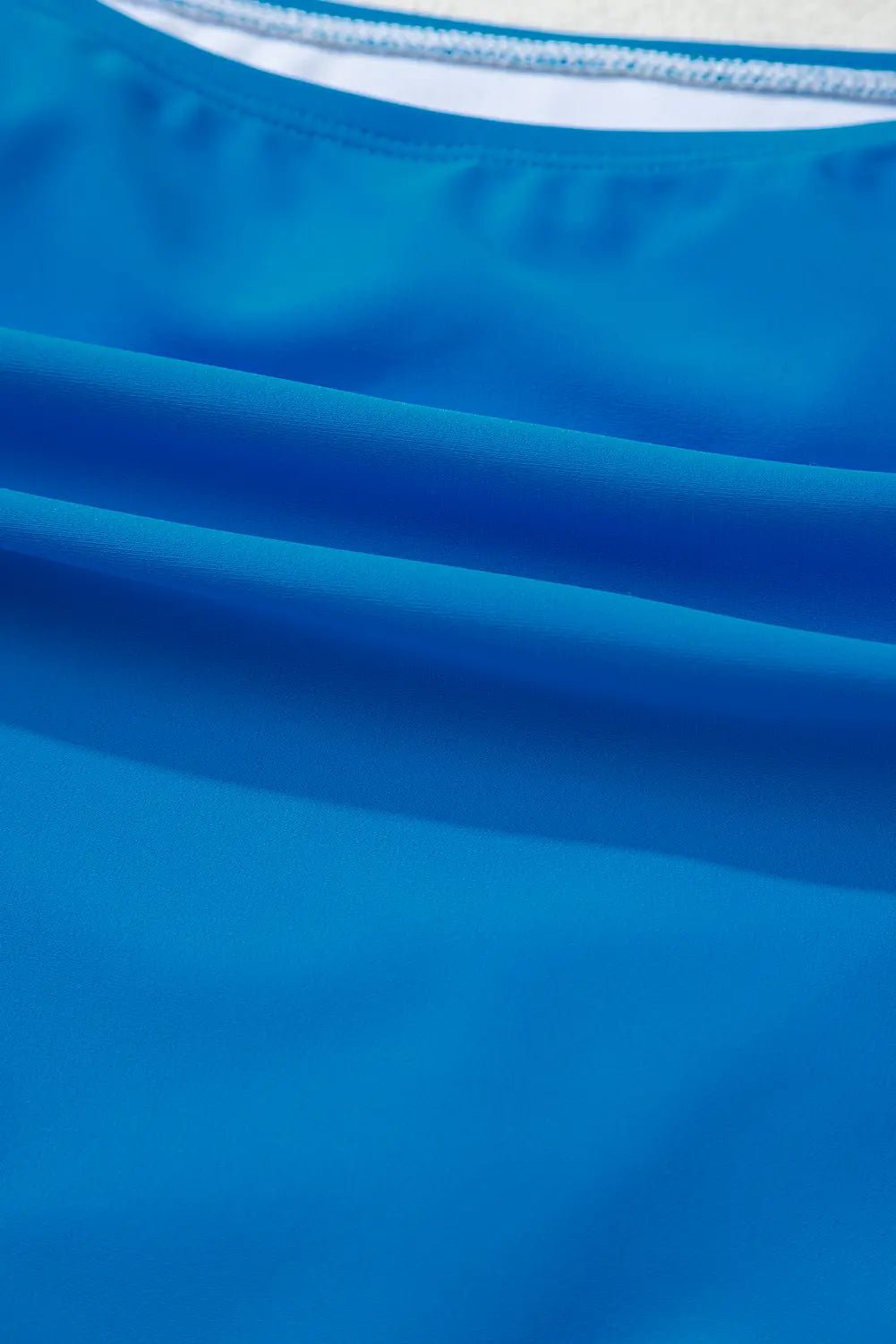 Close-up of a bright blue fabric garment, showing the texture and a sliver of a white inner collar.