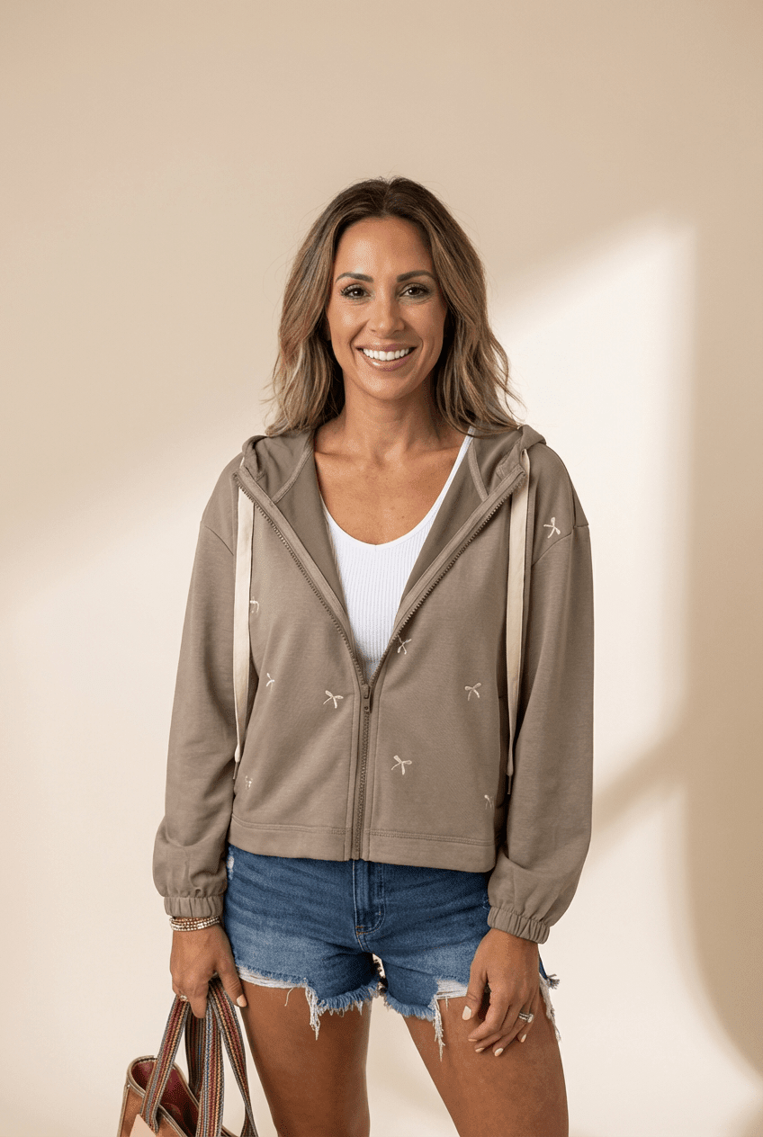 Woman wearing a beige hoodie with star patterns, white shirt, and denim shorts against a beige background