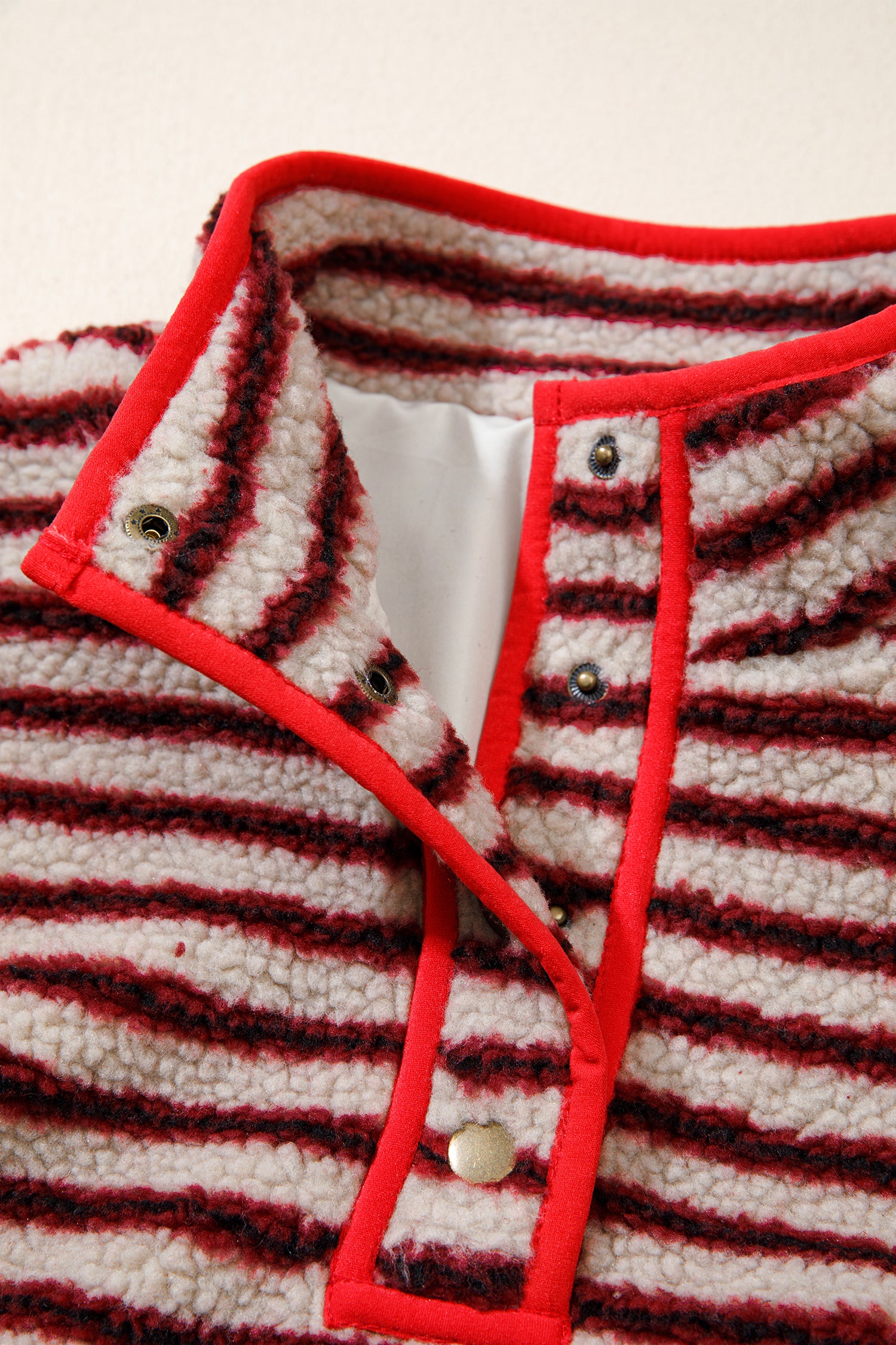 Close-up of red bound stand collar, snaps and lining on striped sherpa pullover
