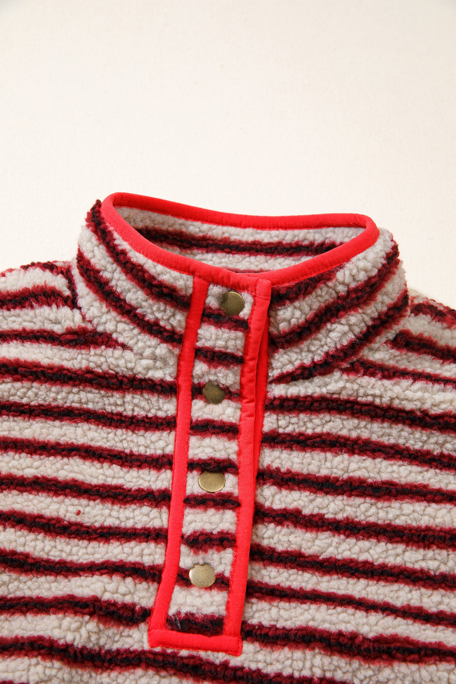 Close-up of snap button placket and red trim on striped sherpa pullover