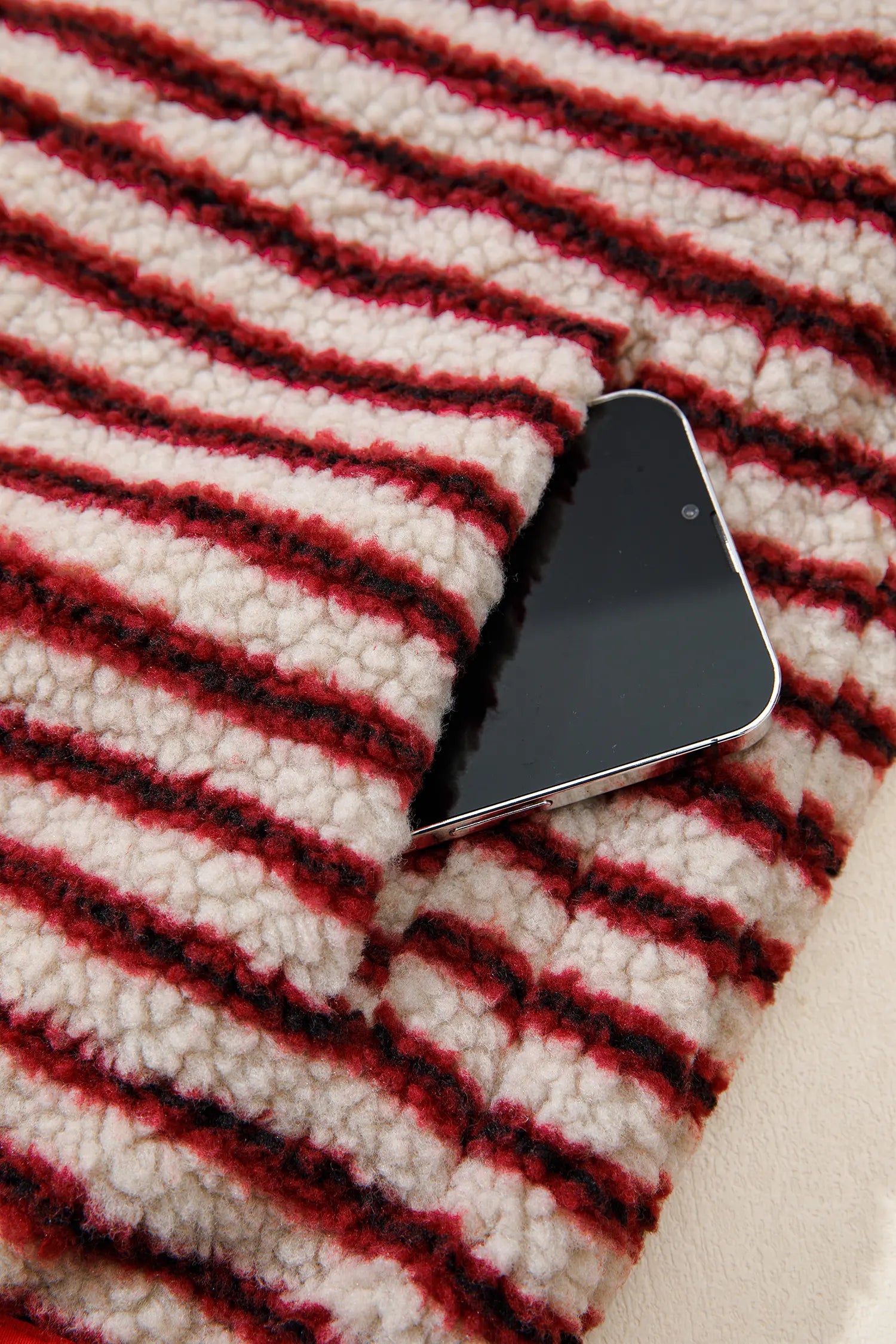 Close-up of side seam pocket holding a phone on red striped sherpa pullover