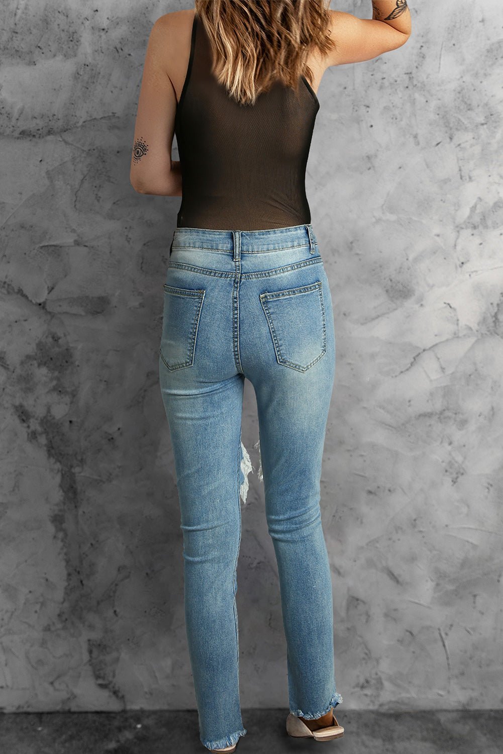 Person wearing blue jeans and a black tank top against a gray concrete wall.