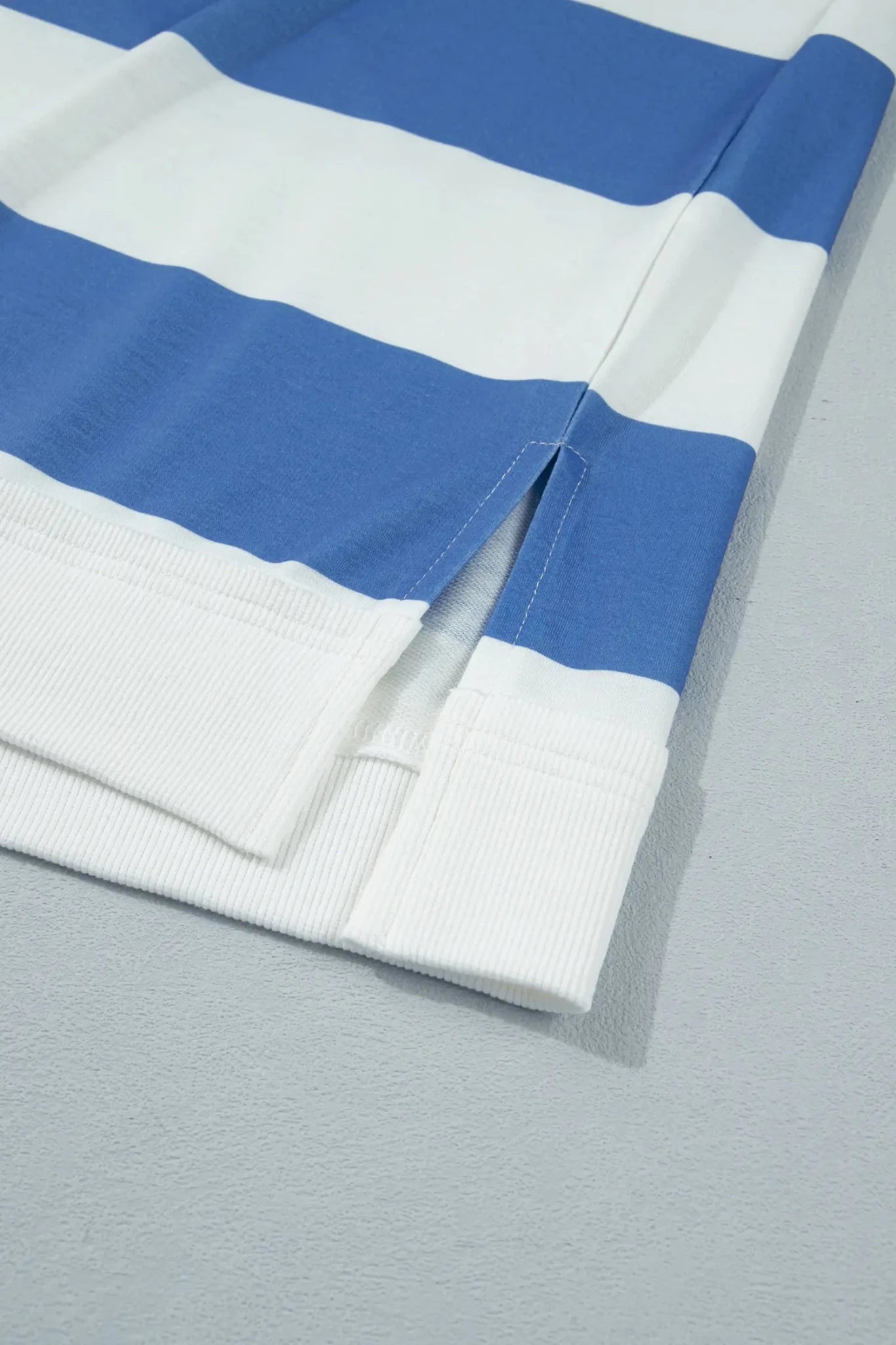 Blue and white striped knit fabric with ribbed cuff on gray surface.