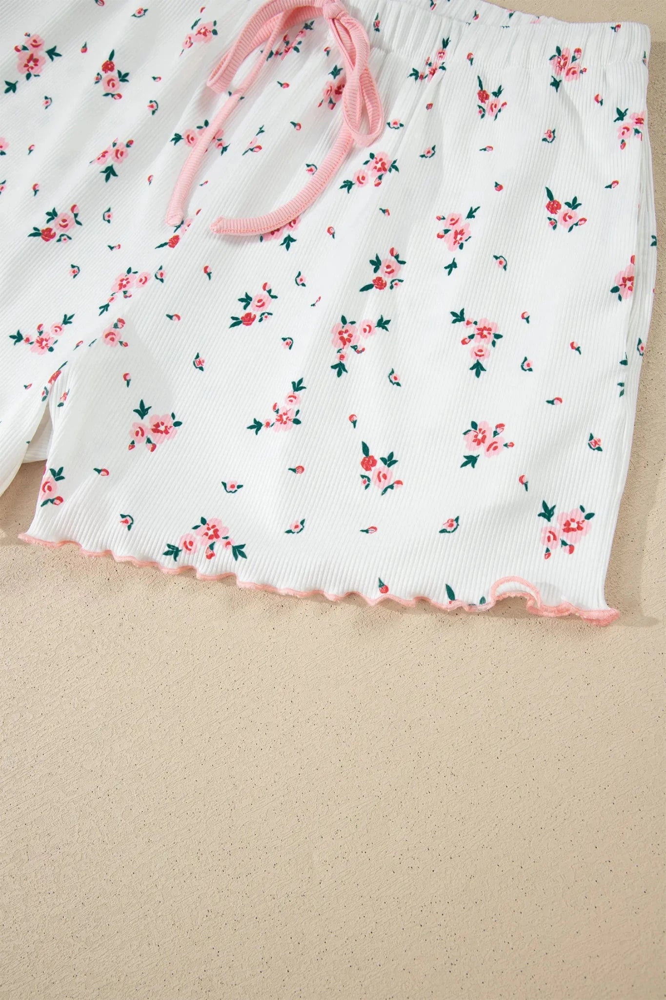 Floral-patterned shorts with a pink drawstring on a beige surface