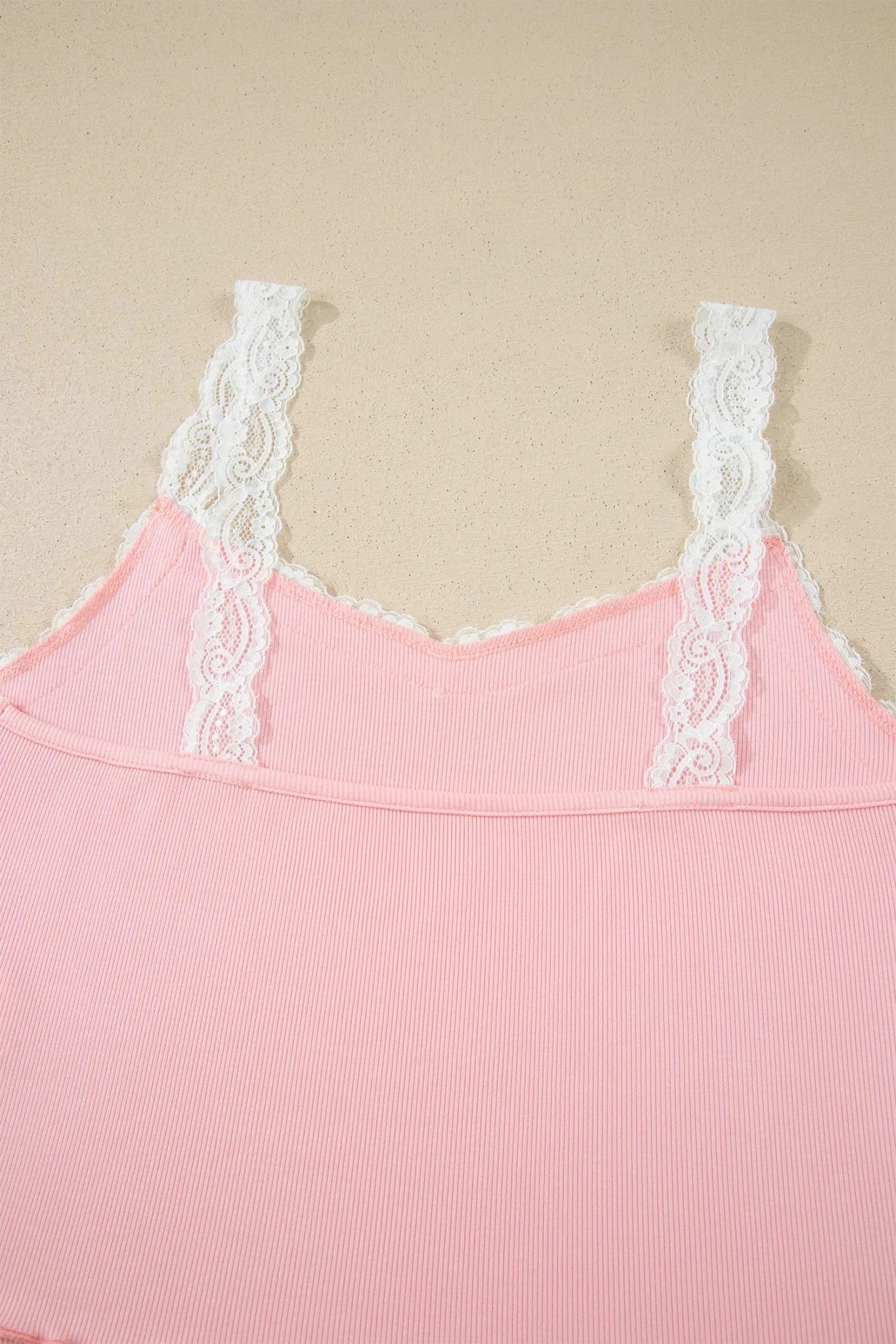 Light pink ribbed camisole with white lace trim on a beige background.