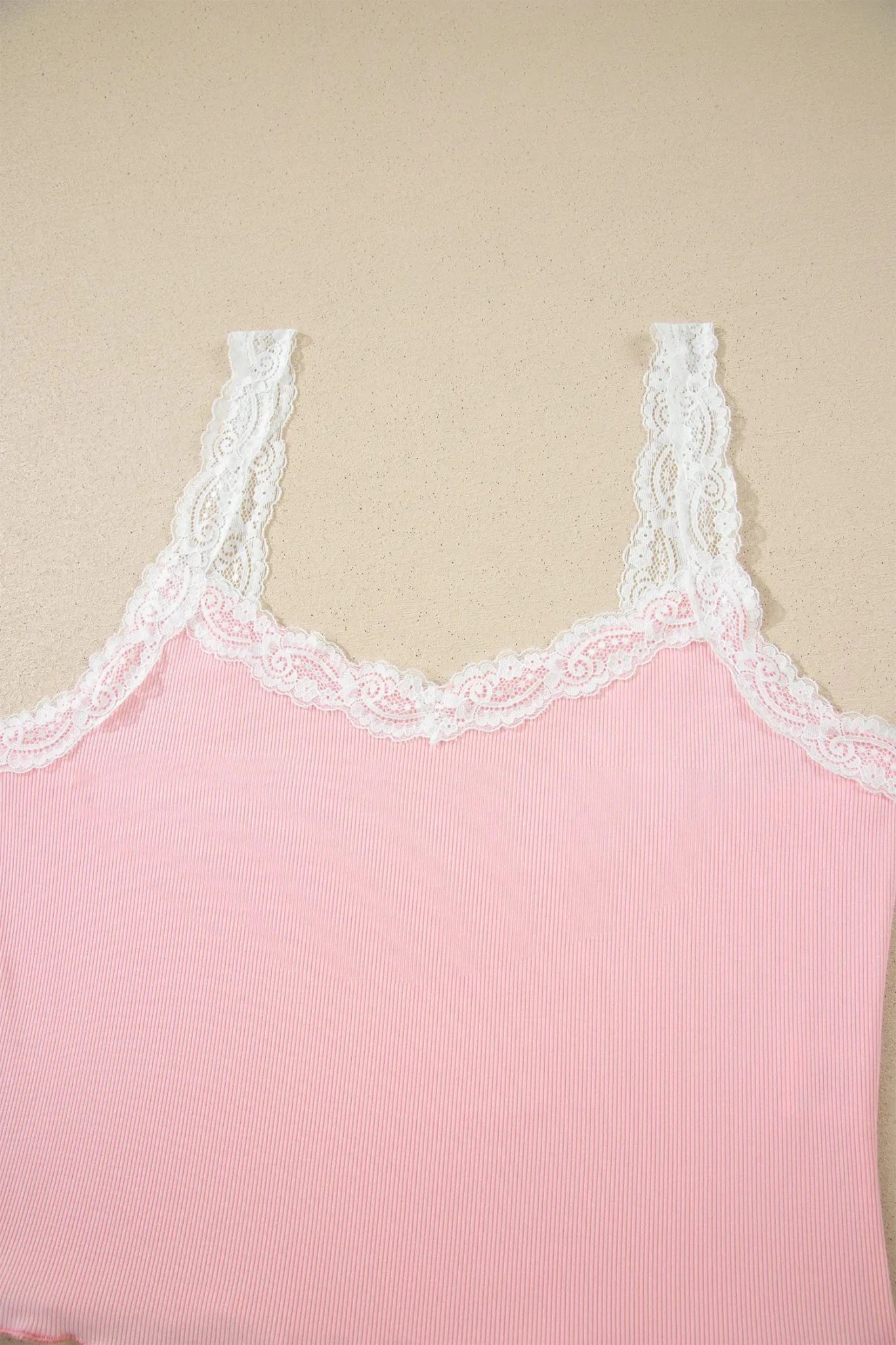 Close-up of a pink ribbed camisole with white floral lace trim on a beige background.