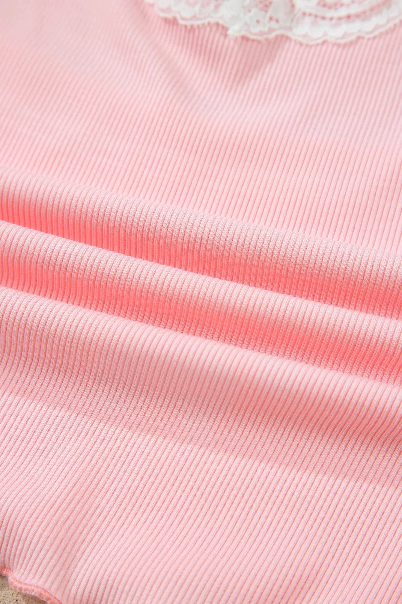 A close-up of a light pink ribbed fabric with a white lace trim visible at the top edge.