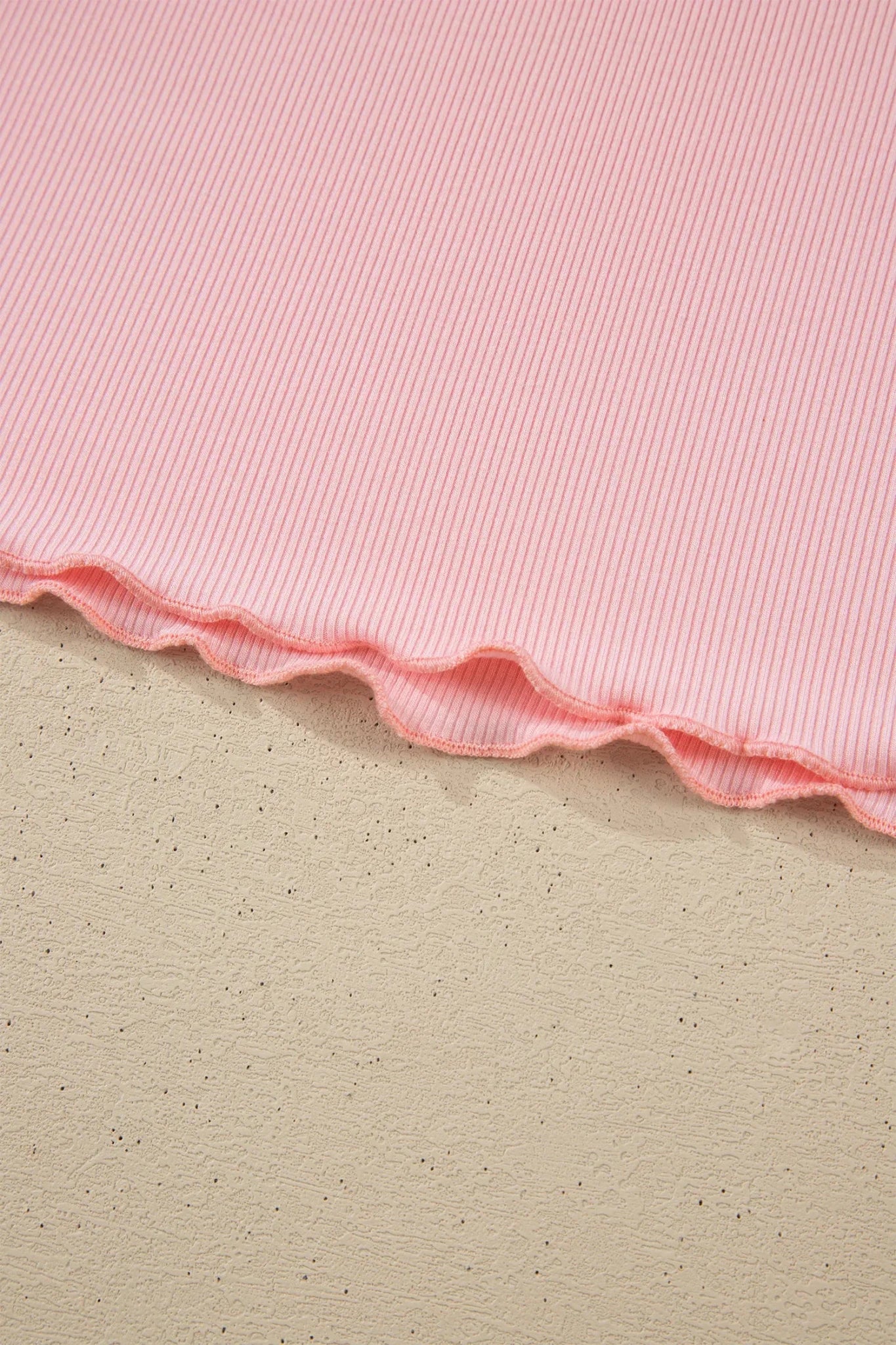 Close-up of light pink ribbed fabric with a scalloped edge.