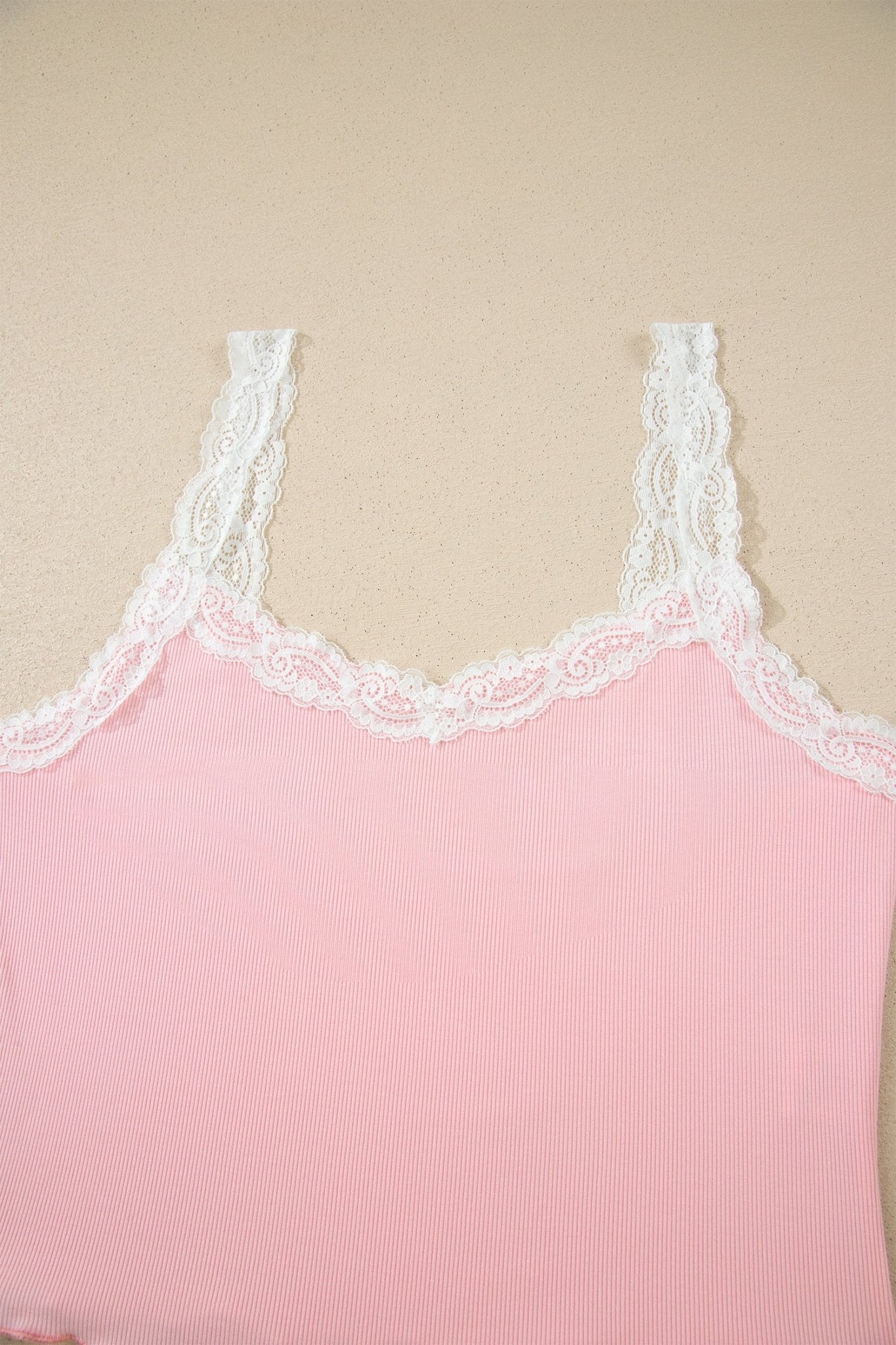 Pink ribbed tank top with lace trim on a beige background