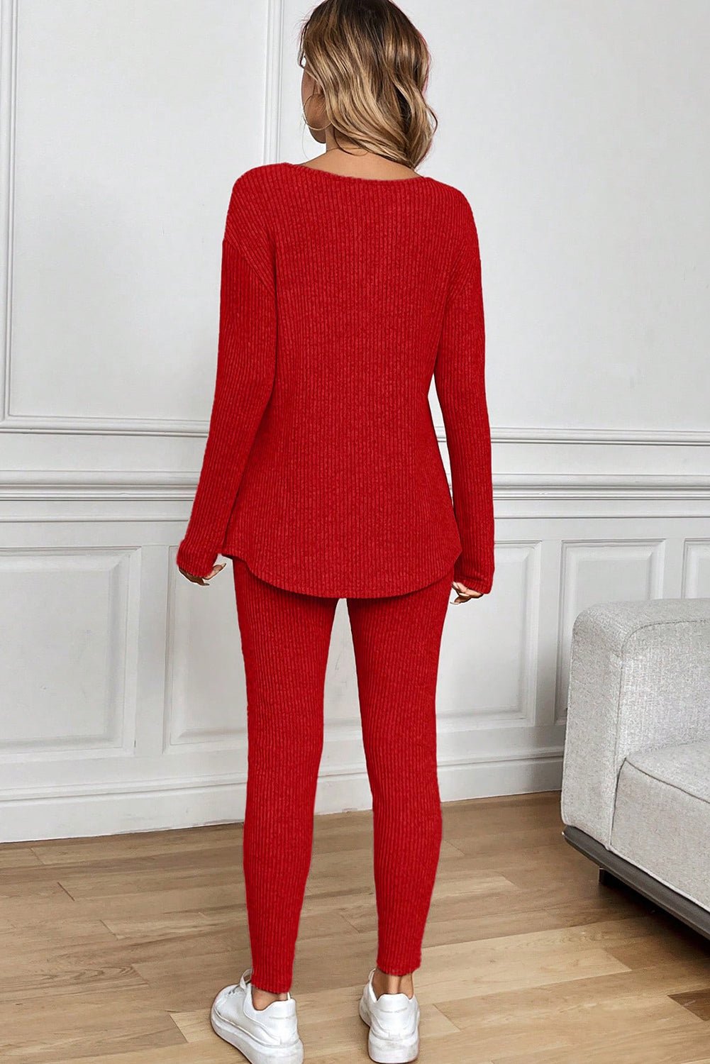 Person wearing a red knit outfit standing in a room with white walls and wooden flooring.
