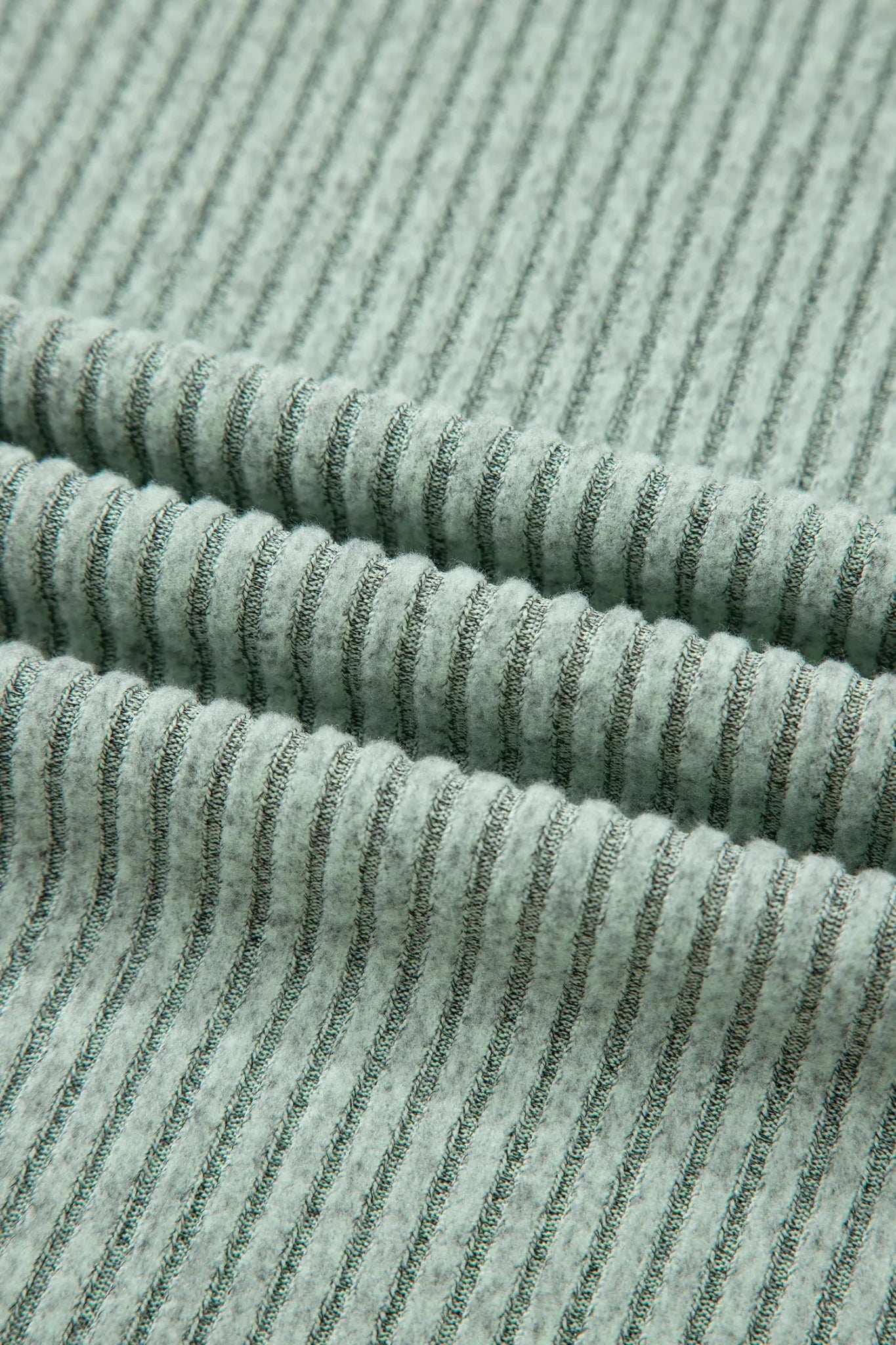 Close-up of pale sage green ribbed knit fabric with darker green stripe