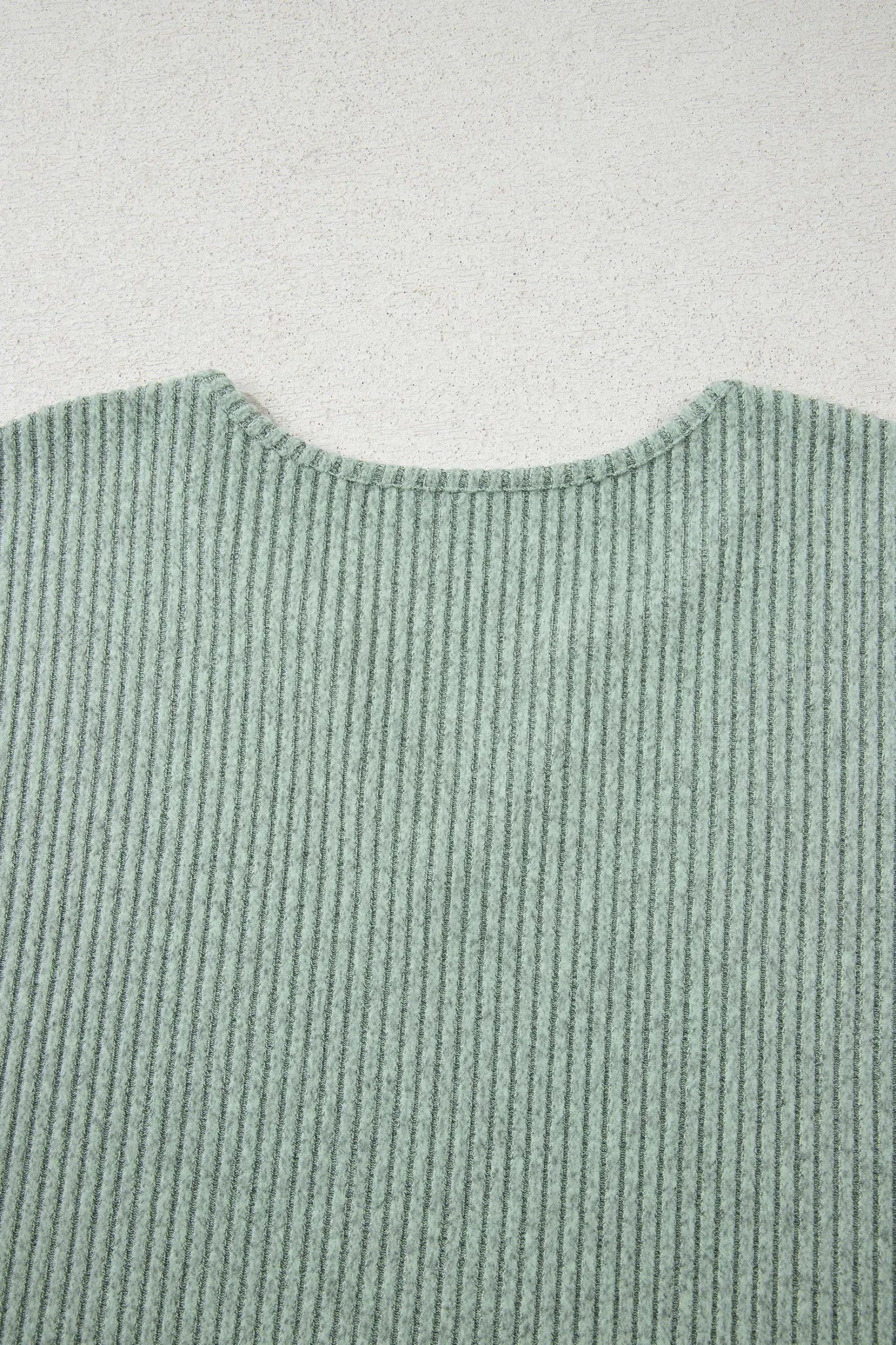 Close-up of muted sage green ribbed sweater showing textured neckline.