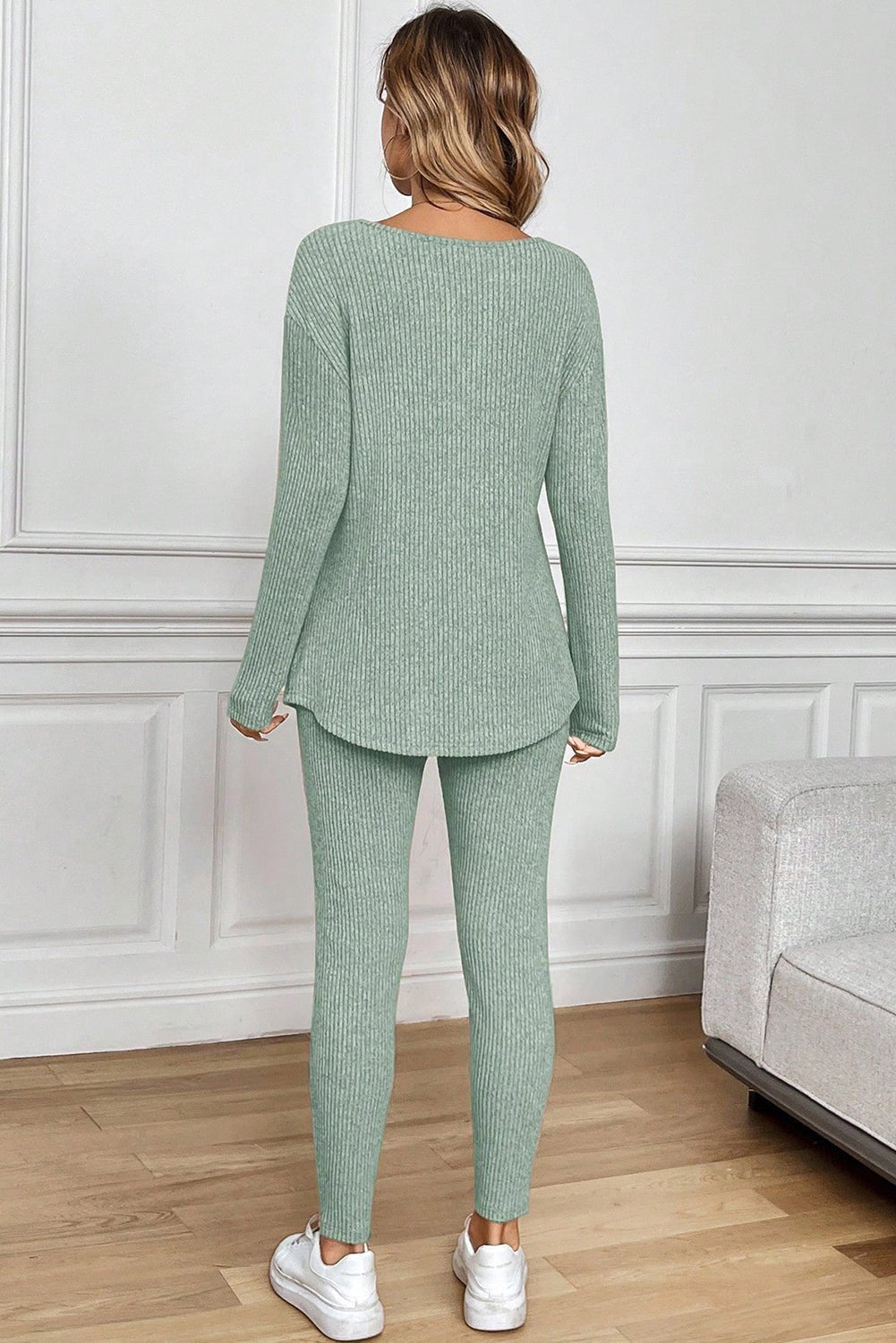 Woman wearing a green ribbed outfit in a room with white walls and wooden flooring.