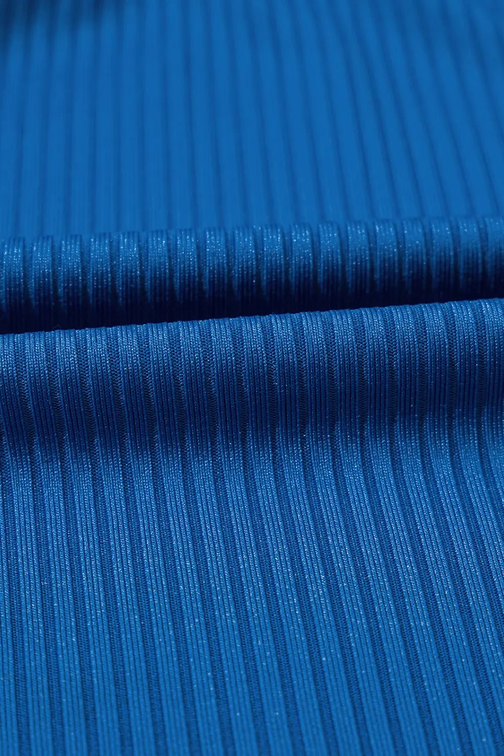 A close-up of bright blue ribbed fabric with a fine vertical texture and a horizontal fold running across the center.